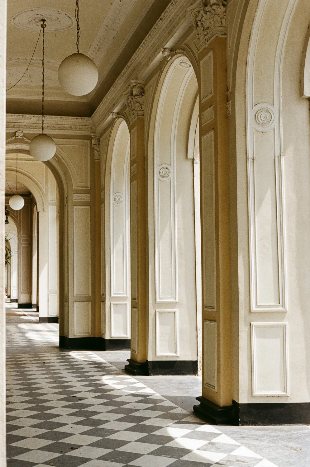 Corridoio con archi eleganti, pareti decorate e lampadari sospesi in un ambiente storico.