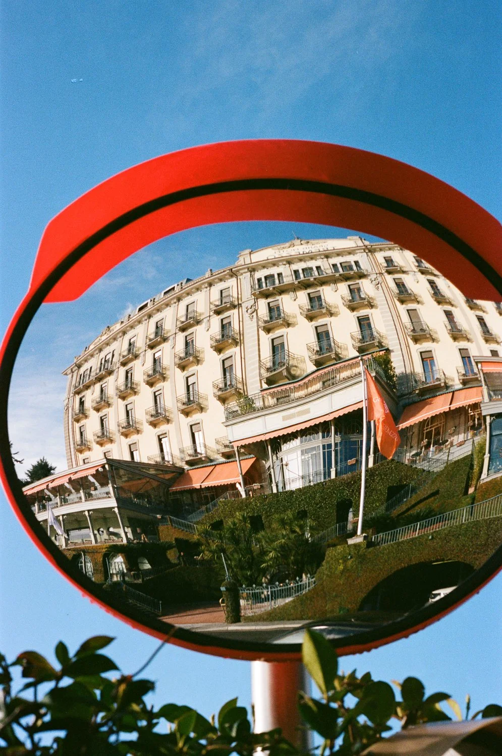Edificio elegante con balconi, riflesso in uno specchio rotondo rosso, sotto cielo blu.
