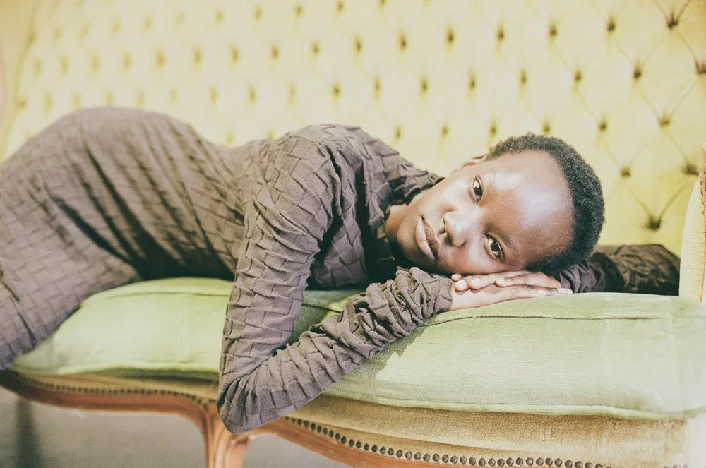 Ragazzo sdraiato su un divano verde, con sfondo giallo, guarda verso l'obiettivo con espressione pensierosa