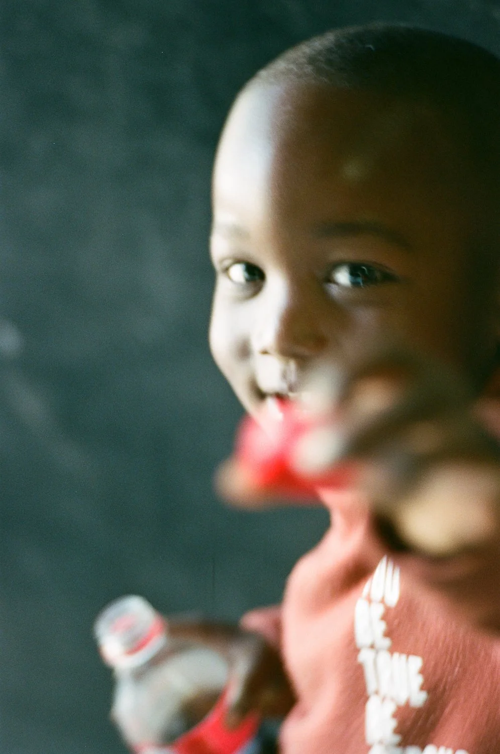 Ragazzo sorridente che tiene una bottiglia di acqua. Sfondo scuro e sfocato.