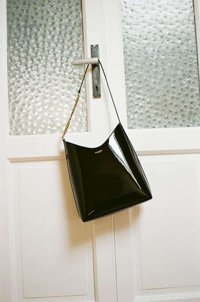 Borsa nera lucida appesa a un pomello di una porta bianca.