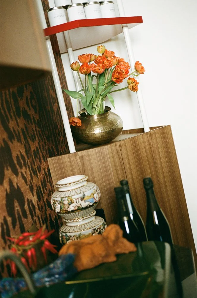 Un'ampia vista di una scaffalatura decorativa con un vaso di fiori arancioni, due bottiglie di vino, e alcune decorazioni.