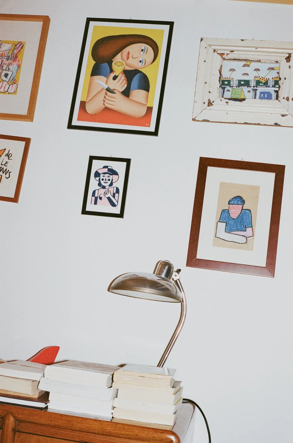 Pittura di una donna con cappello che tiene un limone e un coltello, quadro di una donna con cappello e braccia incrociate, quadro di un paesaggio con case colorate, e quadro di una persona con maglietta blu e testa coperta da una maschera. Sul tavol