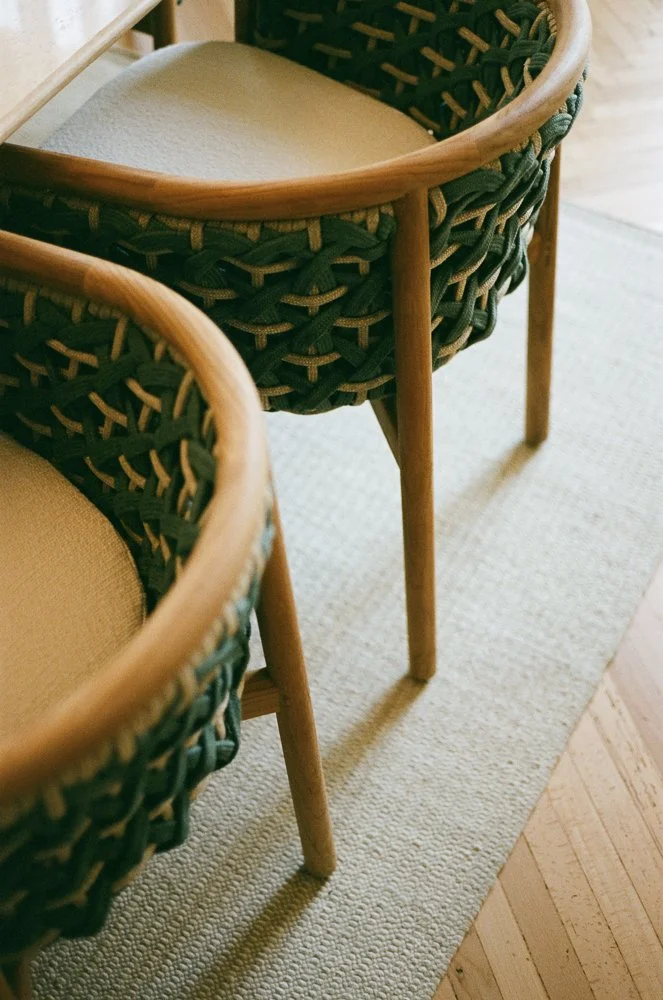 Due sedie di legno con schienale intrecciato in tessuto verde e seduta imbottita beige, posizionate su un tappeto beige in un ambiente domestico.