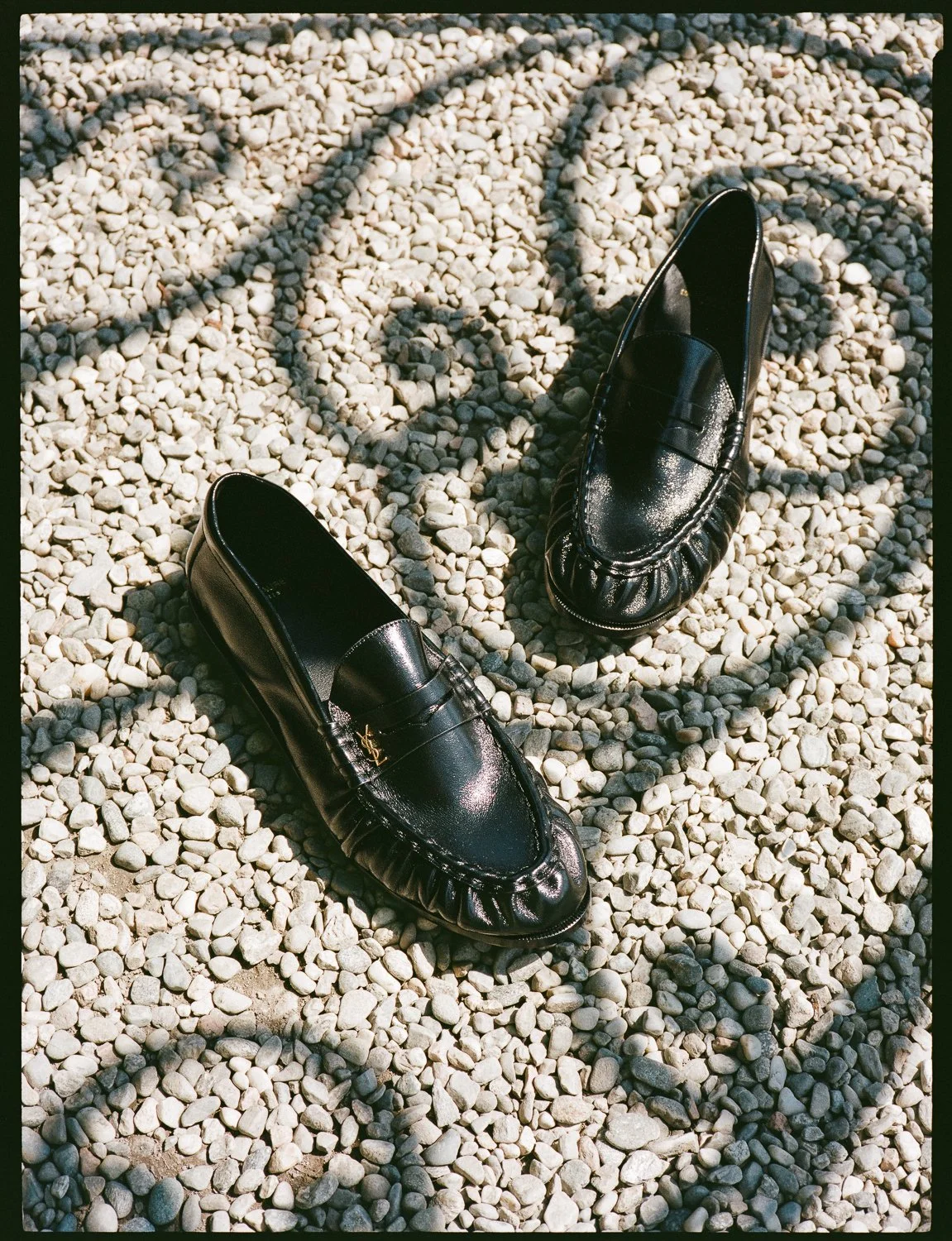 Scarpe nere eleganti su un terreno di ciottoli con ombre proiettate.