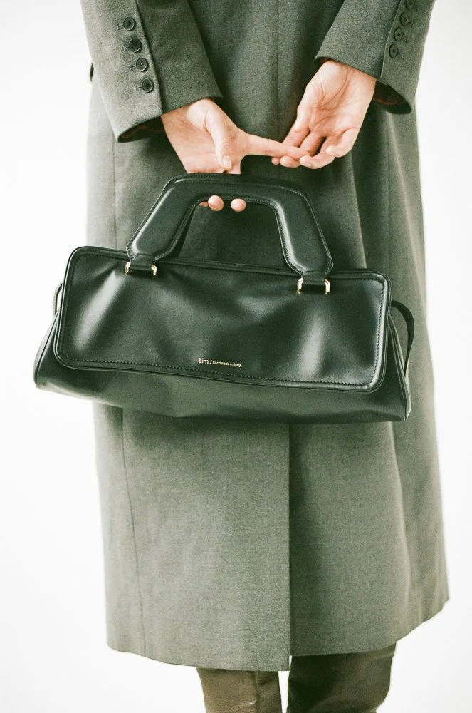 Persona con abito grigio che tiene in mano una maleta nera