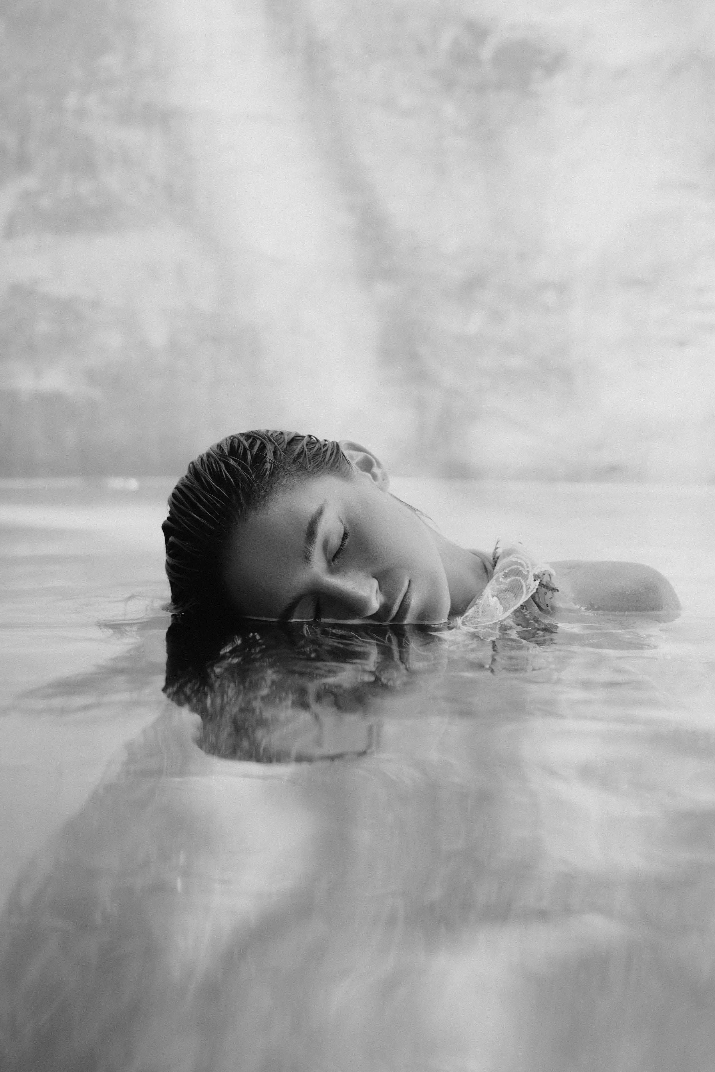 Black and white portrait of a woman with her face partially submerged in water and her eyes closed.