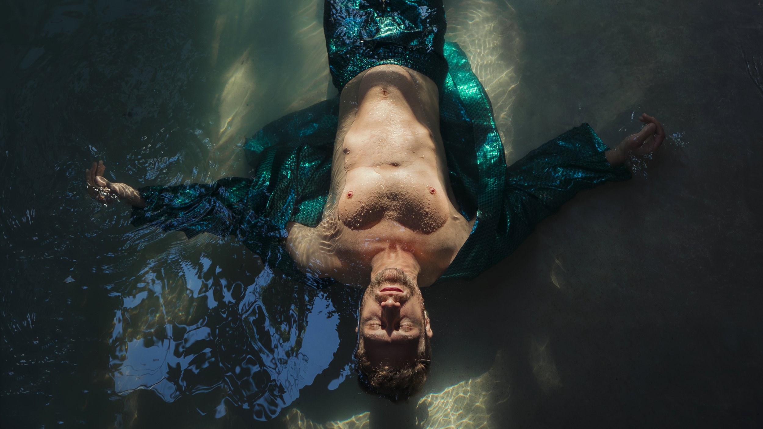 Top-down color portrait of a man floating in the water wearing an open, bright green jacket.