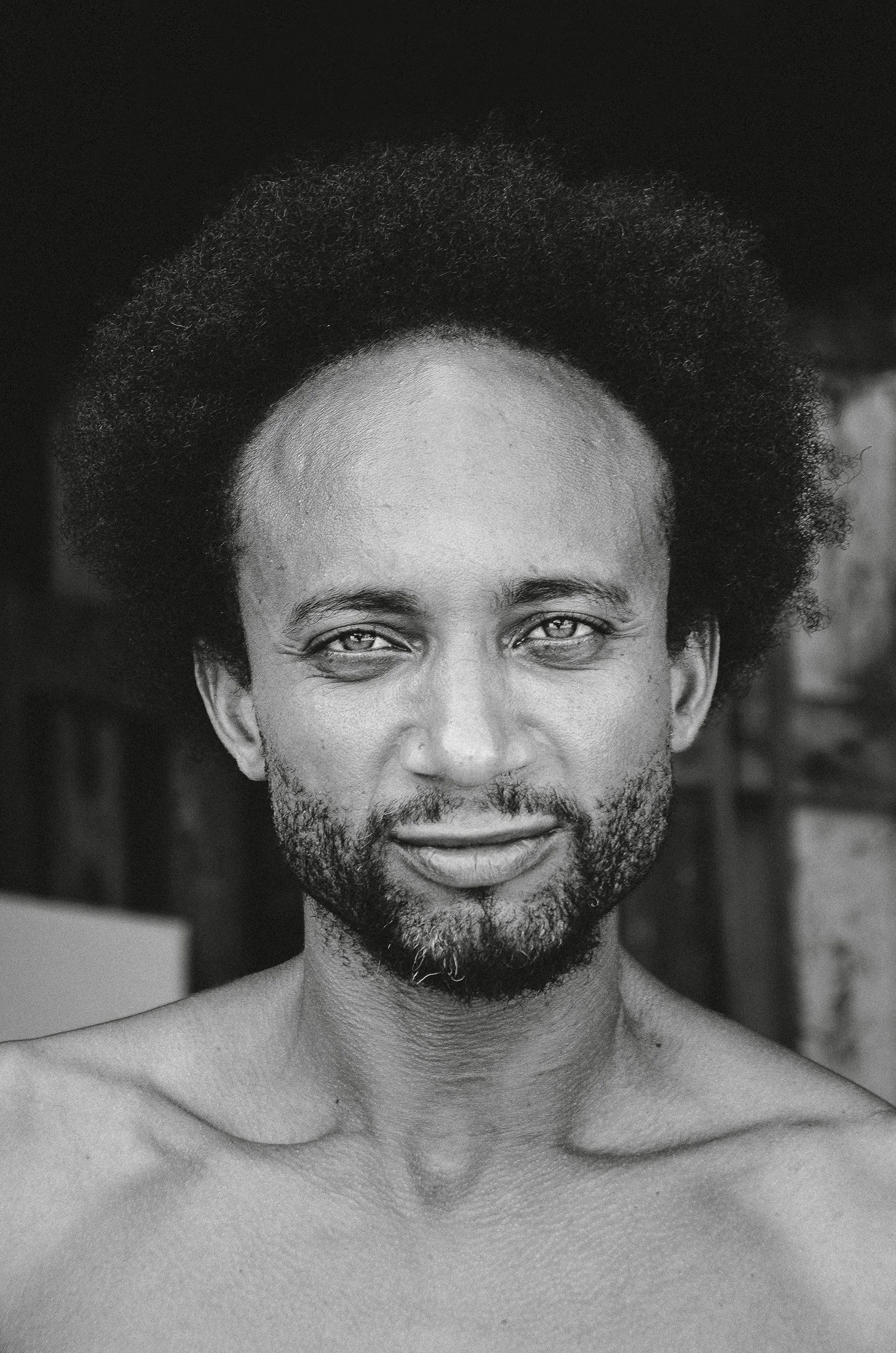 Frontal black and white portrait of a man with a beard and Afro hair, looking directly at the camera.