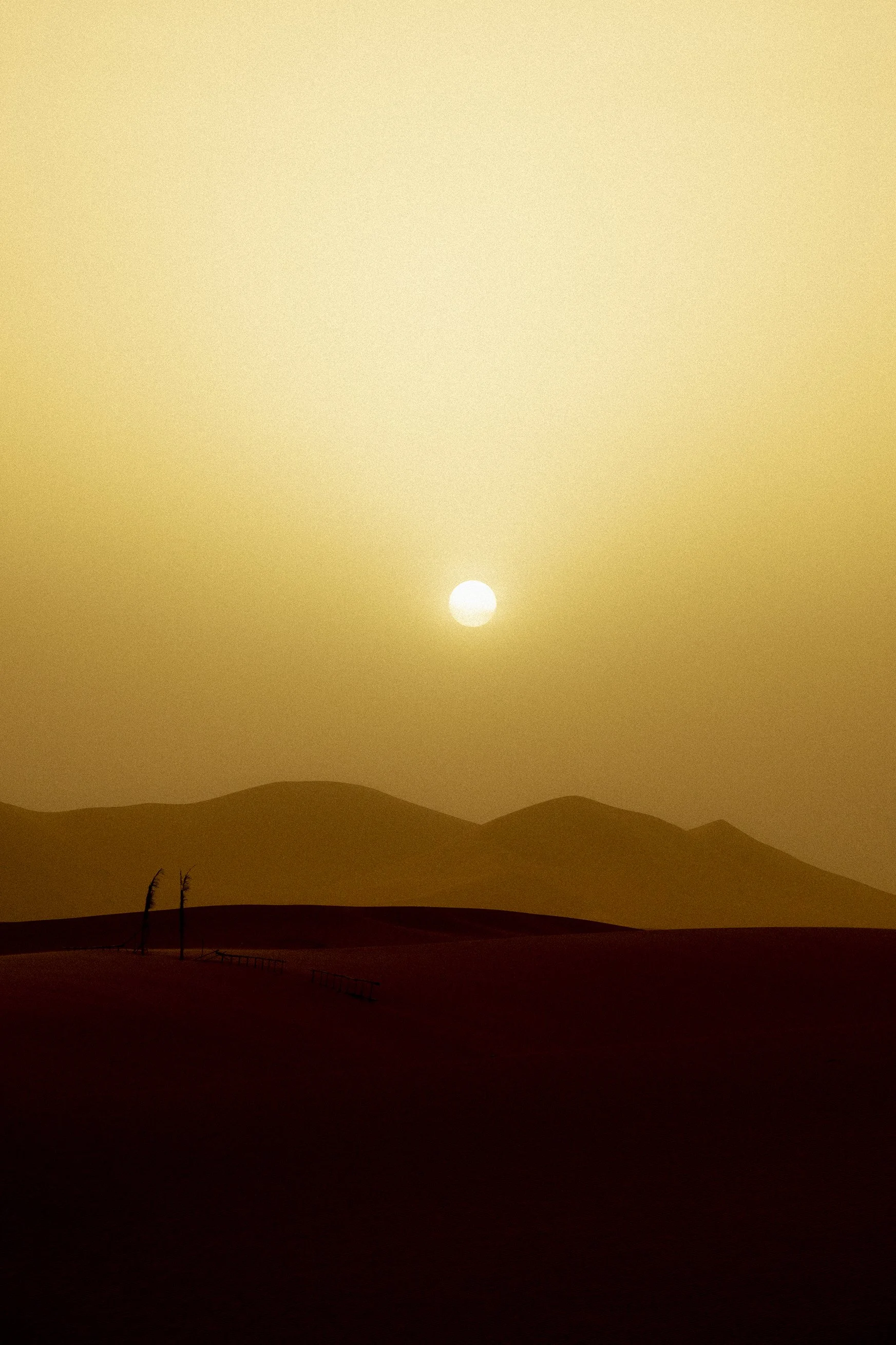 Golden-toned landscape photograph capturing a bright sun descending over the silhouette of desert dunes.