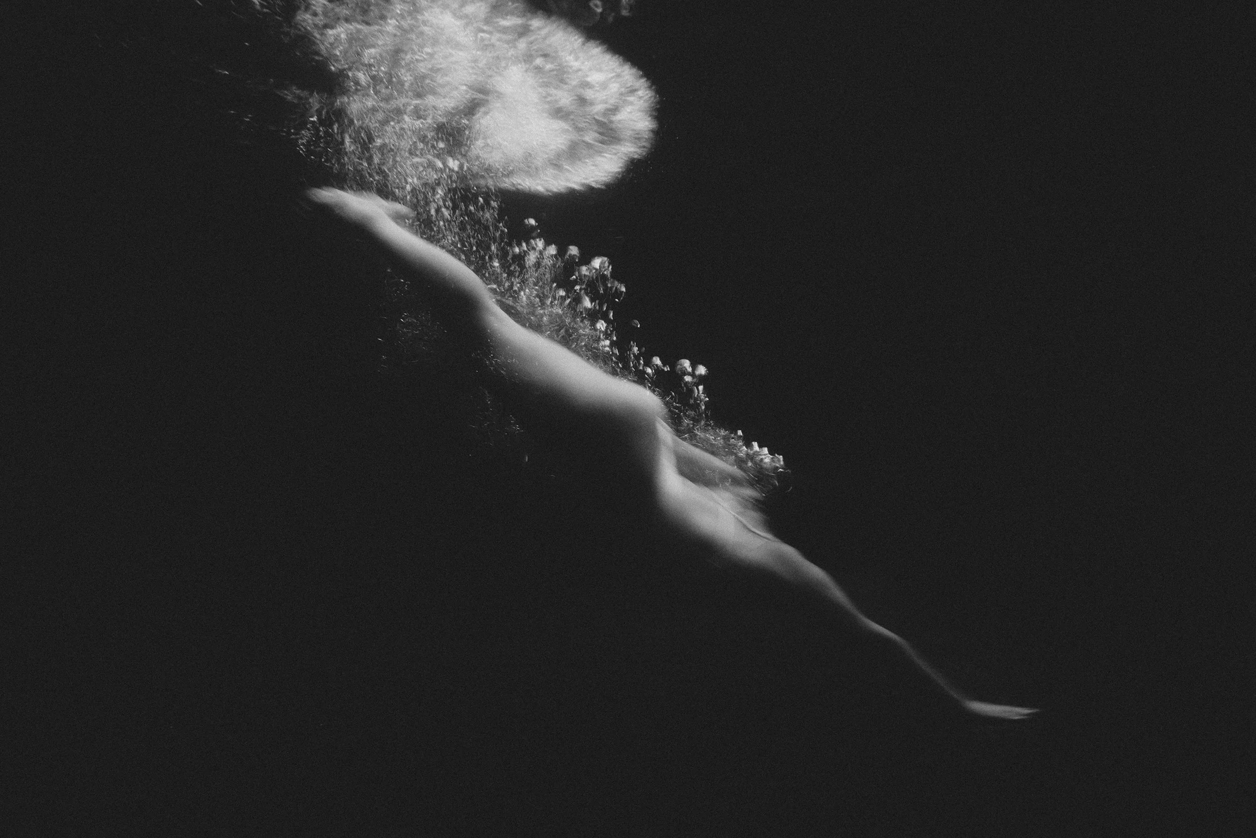Fotografía subacuática en blanco y negro de una figura humana nadando hacia la superficie rodeada de burbujas.