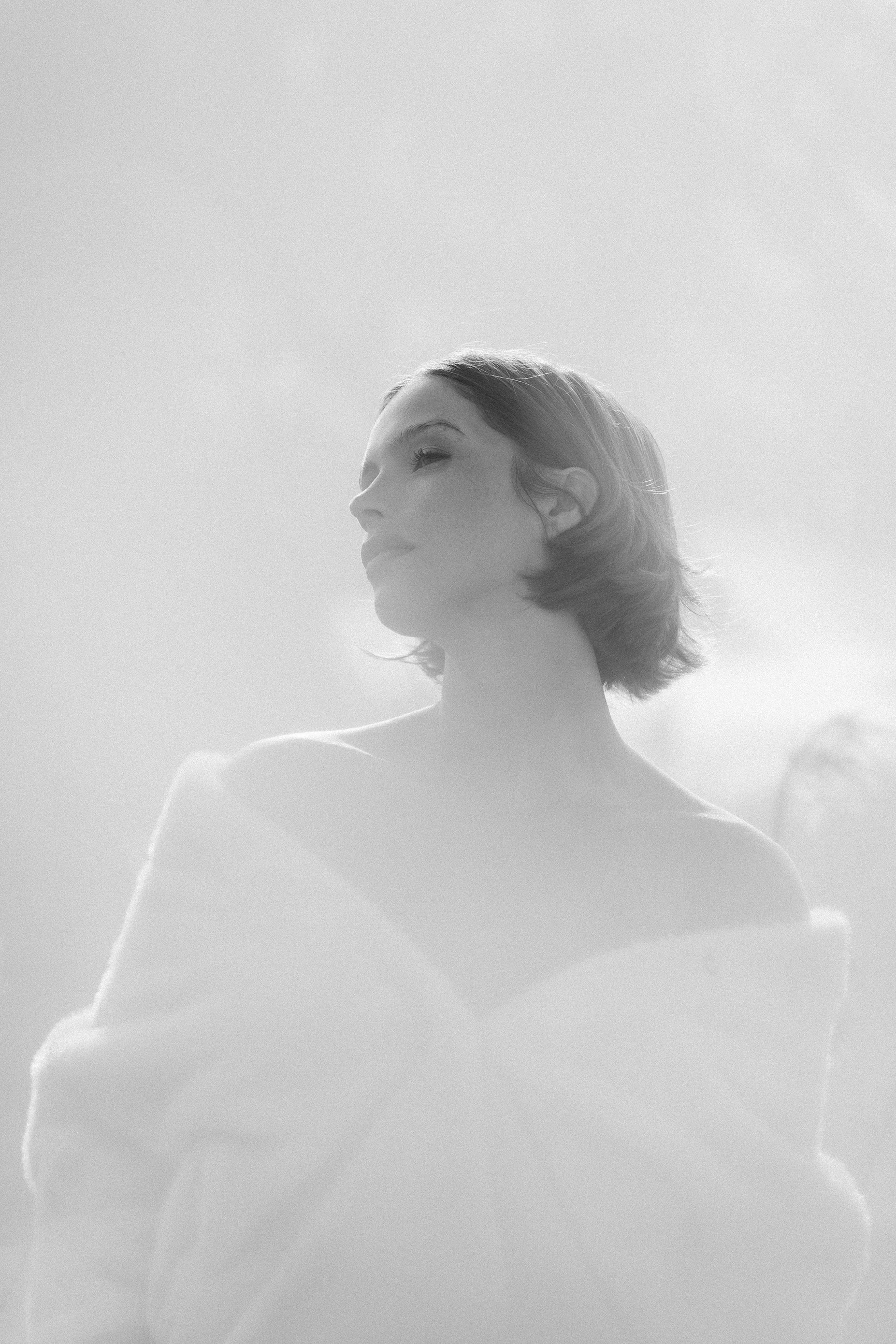 Ethereal black and white portrait of a woman with bare shoulders looking upward.
