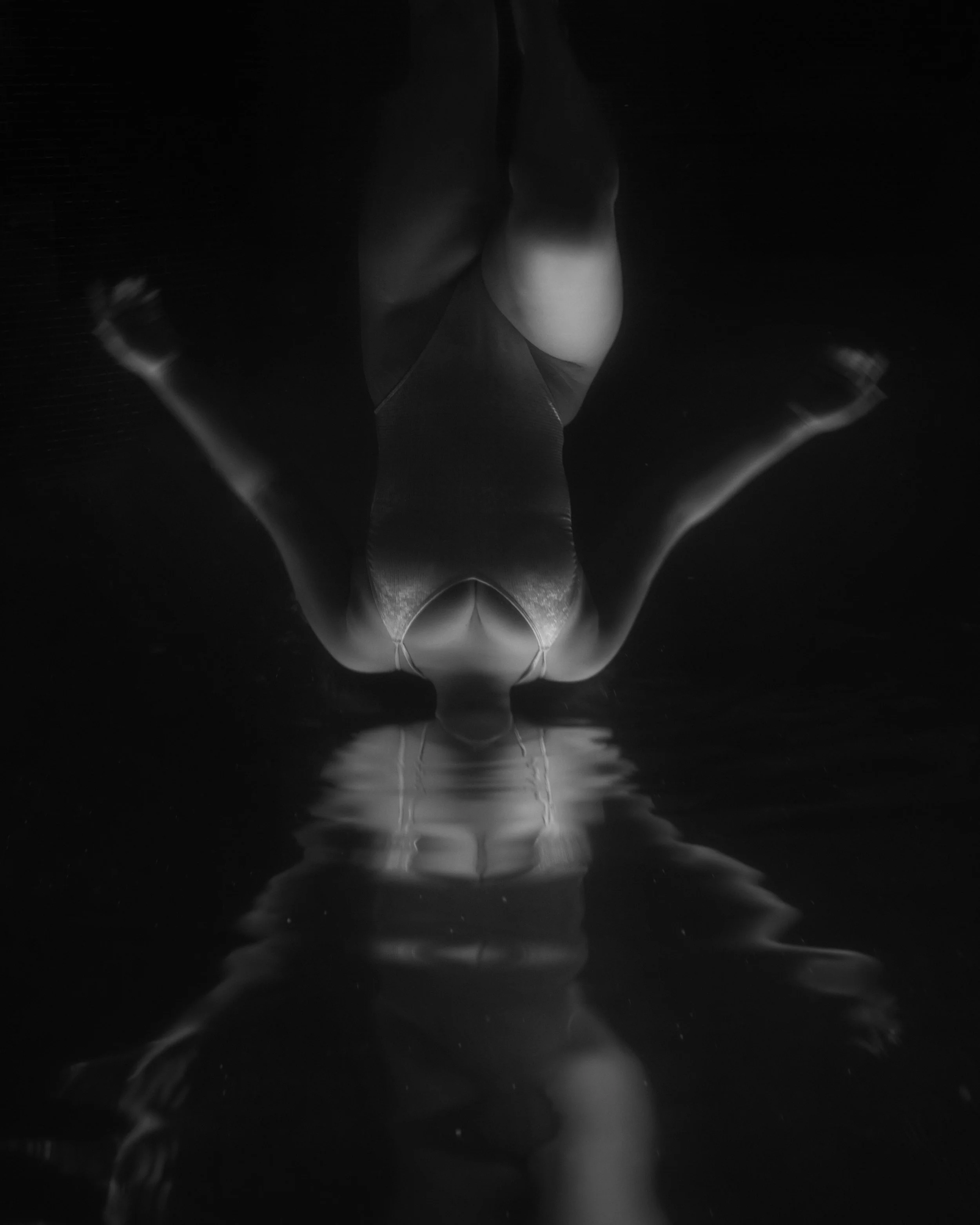Abstract conceptual black and white photograph of an inverted figure reflecting on a dark surface.