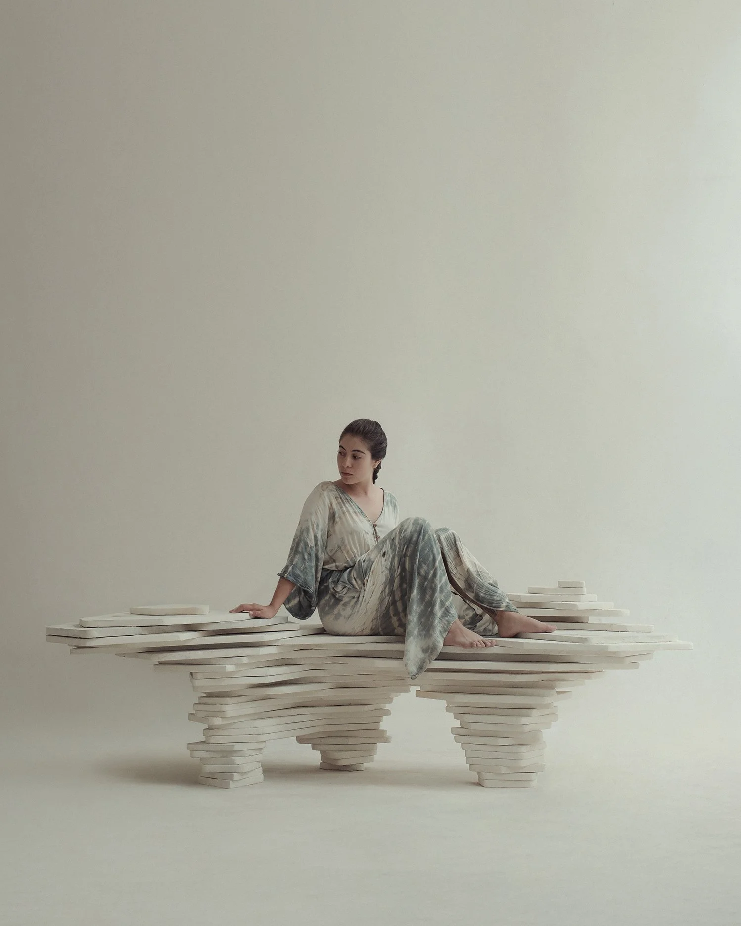 Editorial color photograph of a woman in a patterned dress seated on an organic white sculptural bench.