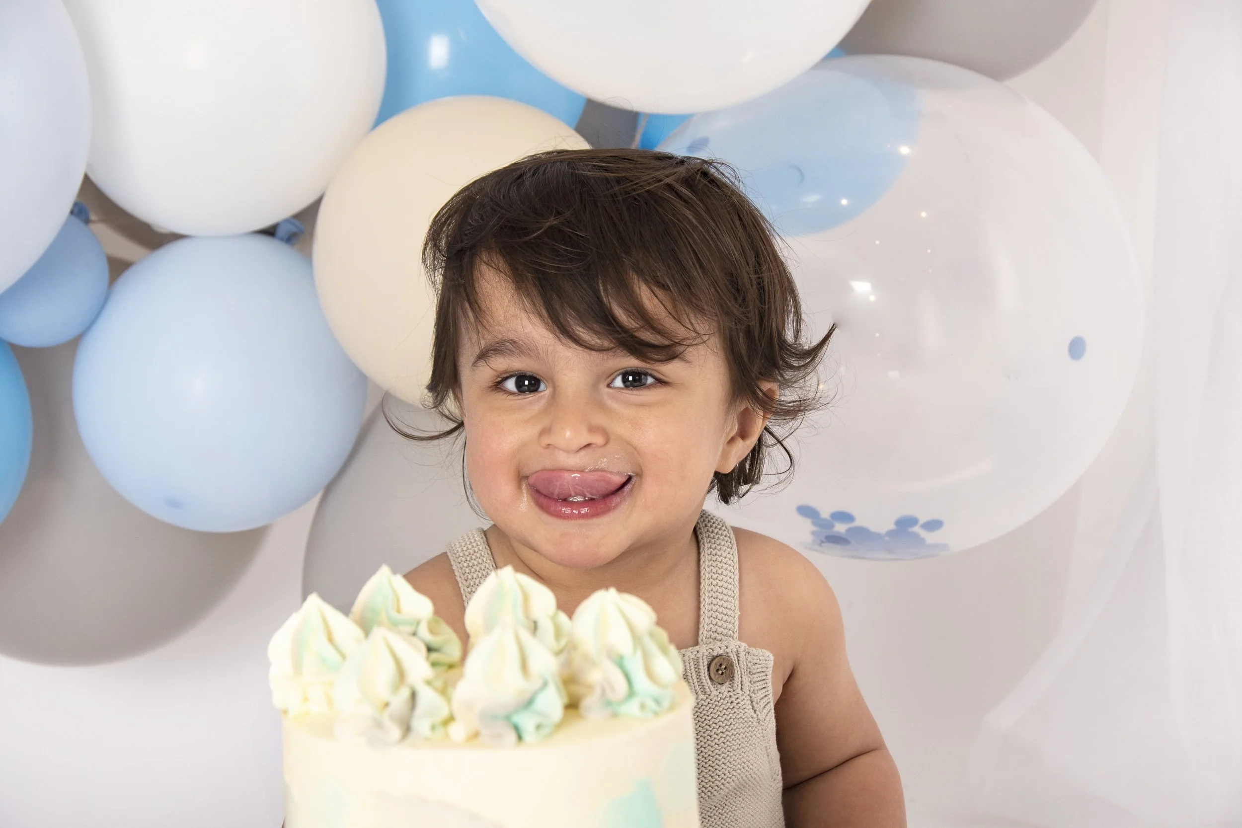 Smiling child with a birthday cake and blue balloons background.