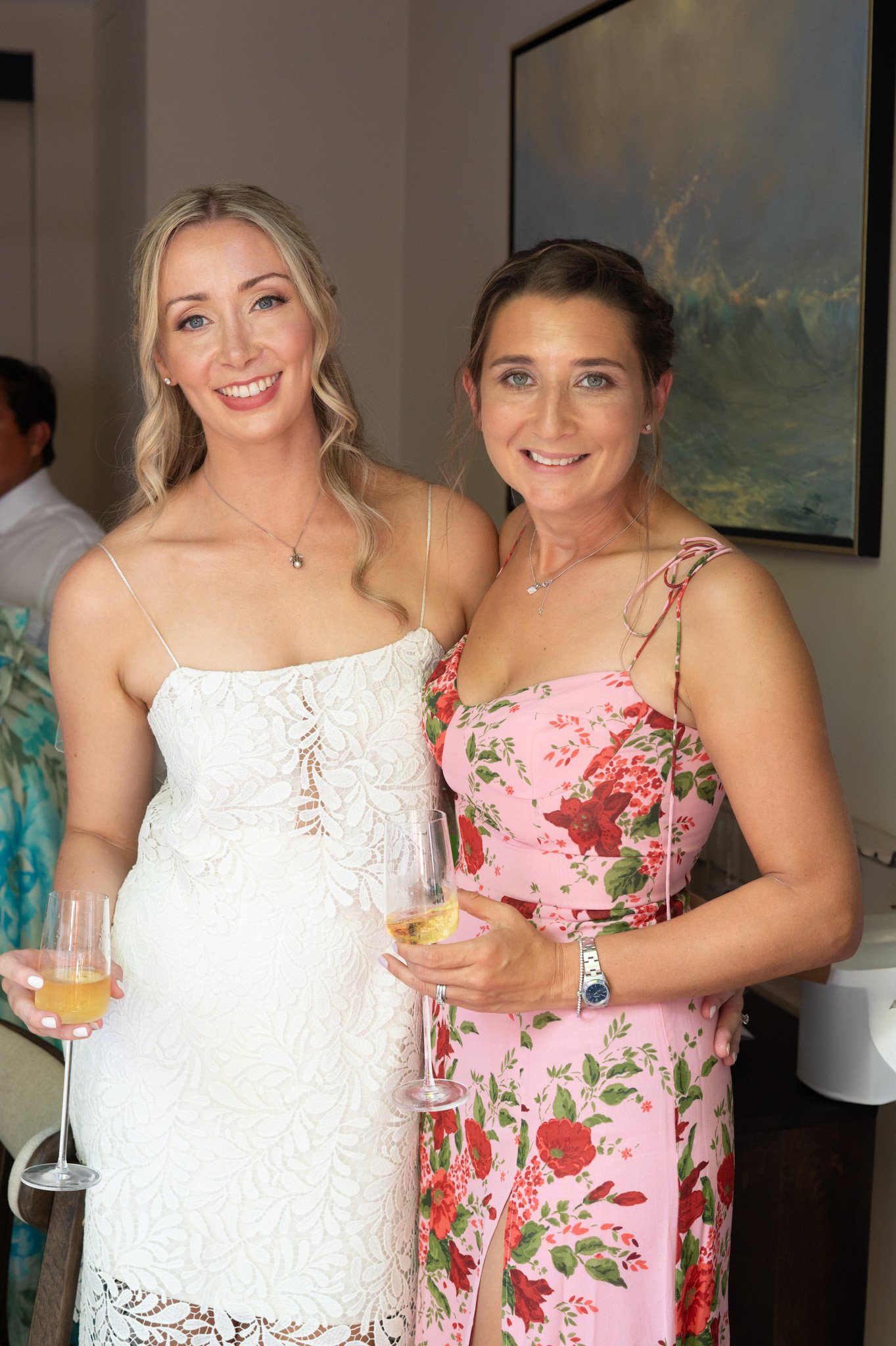 Two women in summer dresses holding glasses of champagne at a celebration