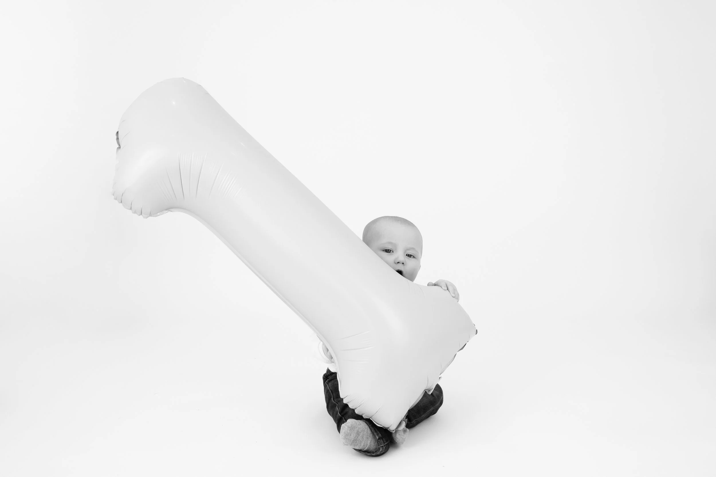 Baby holding large balloon shaped like the number one.