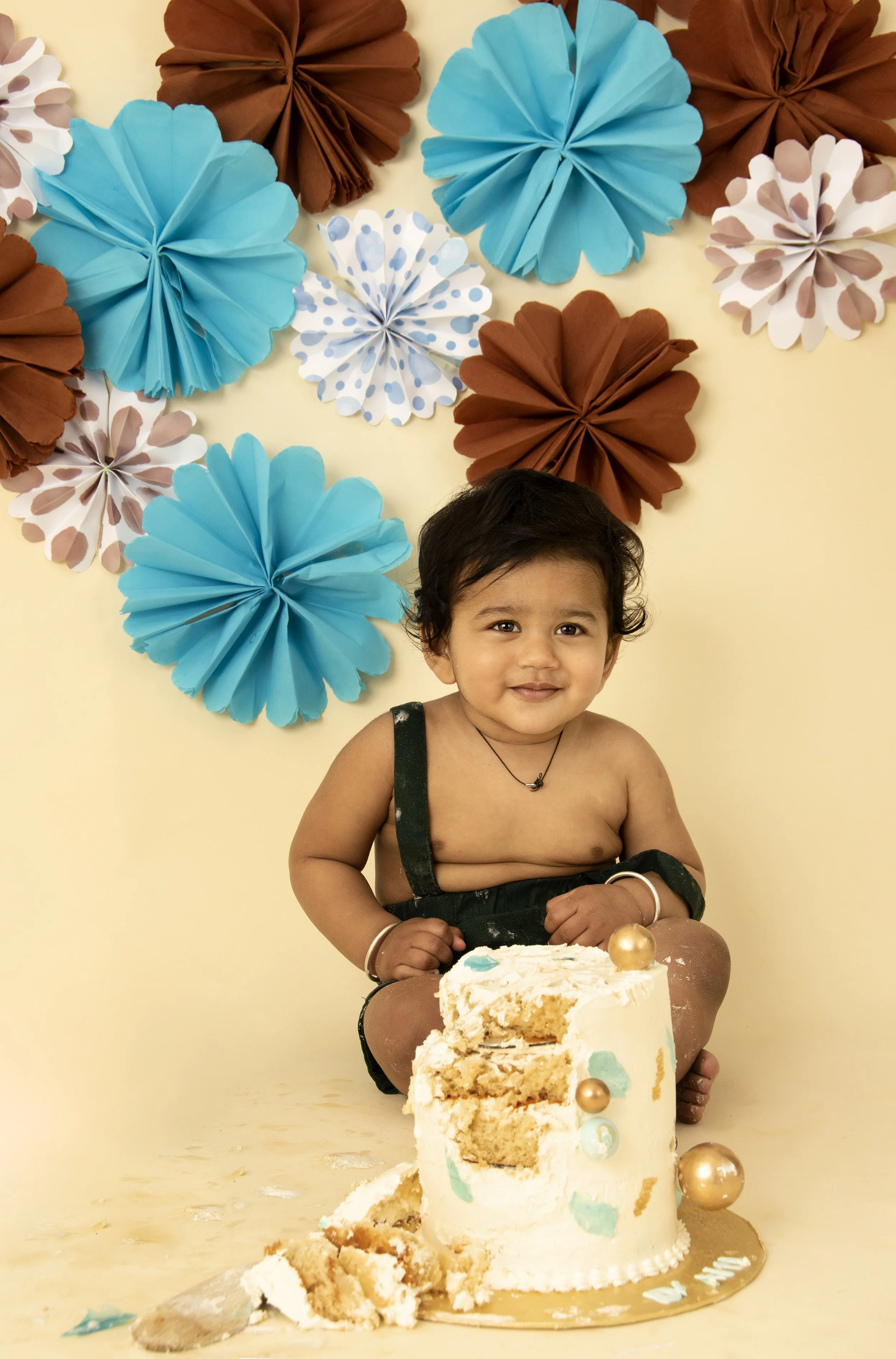 Baby sitting in front of a partially smashed cake with blue and brown paper decorations in the background.