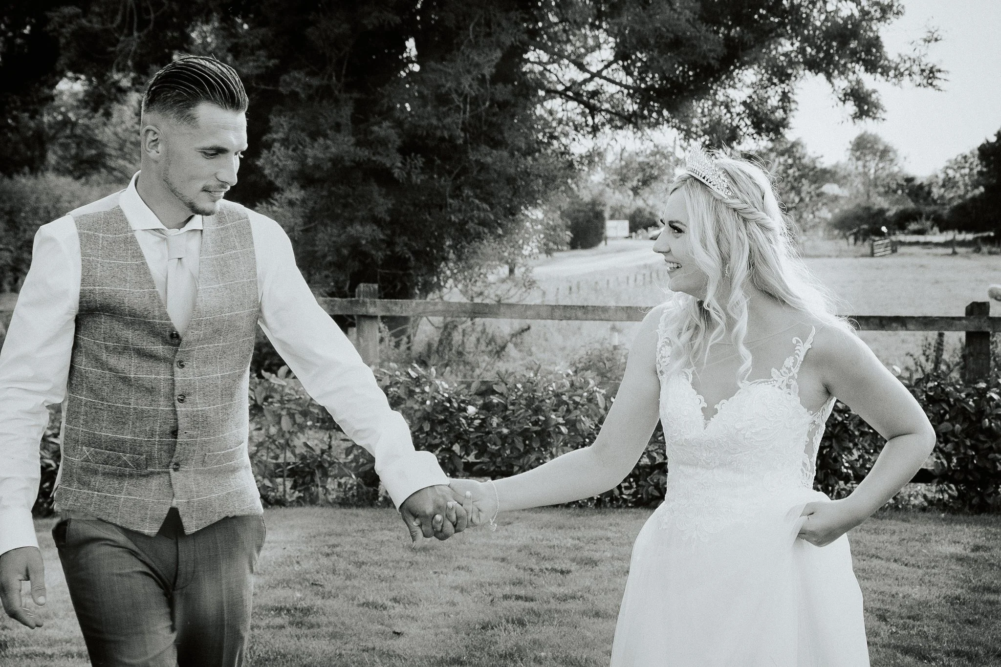 Bride and groom holding hands outdoors in a garden, black and white photo.