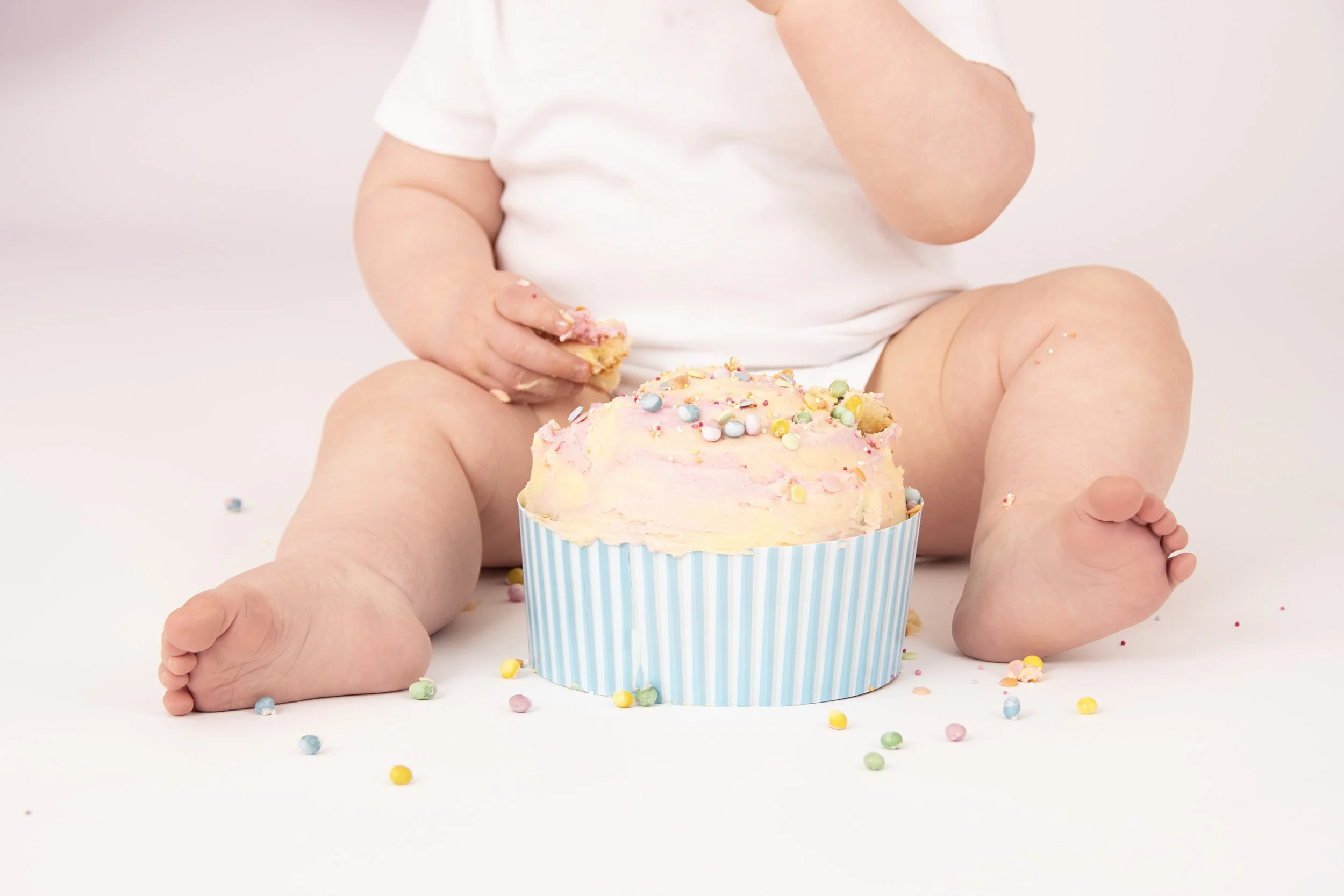 Baby sitting with a frosted cupcake, surrounded by colorful sprinkles.