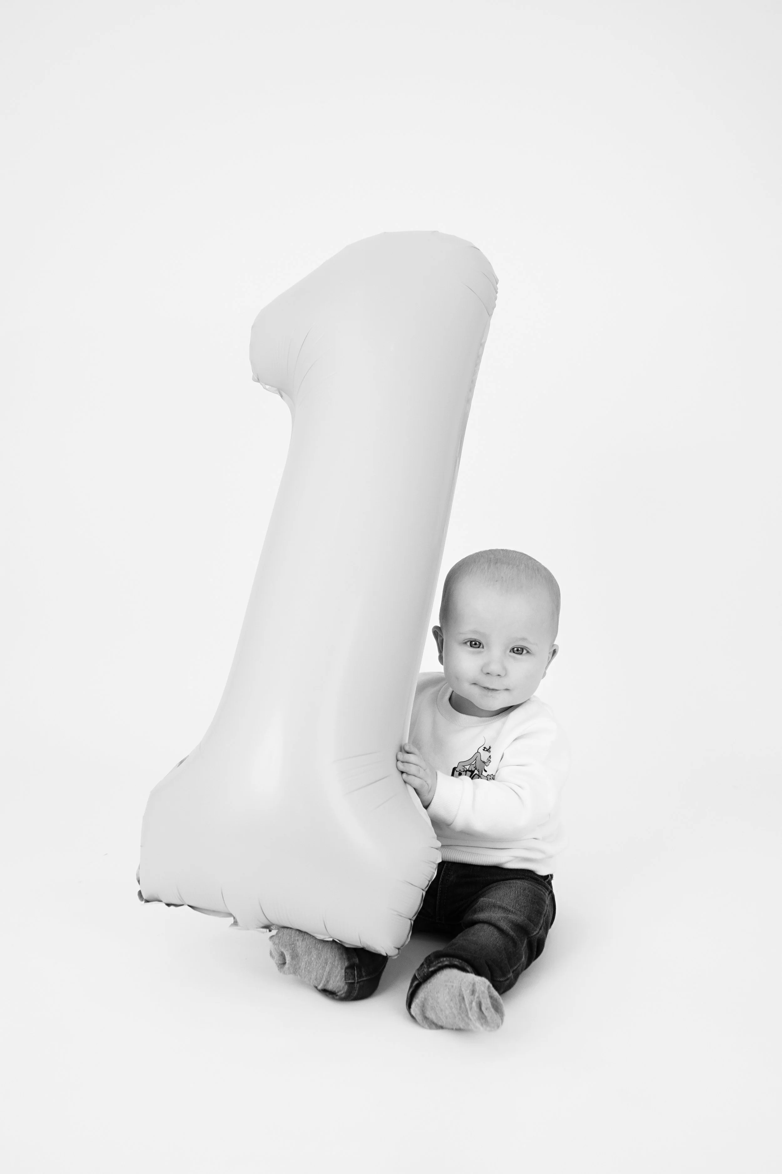 Black and white photo of a baby holding a large inflatable number one.