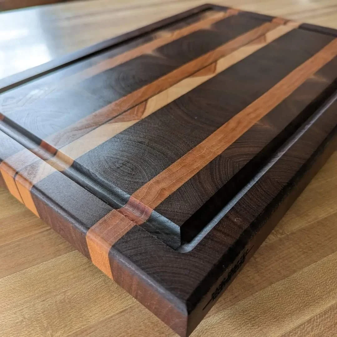 Close-up of a wooden cutting board with a rectangular inset handle, made of dark and light wood strips.