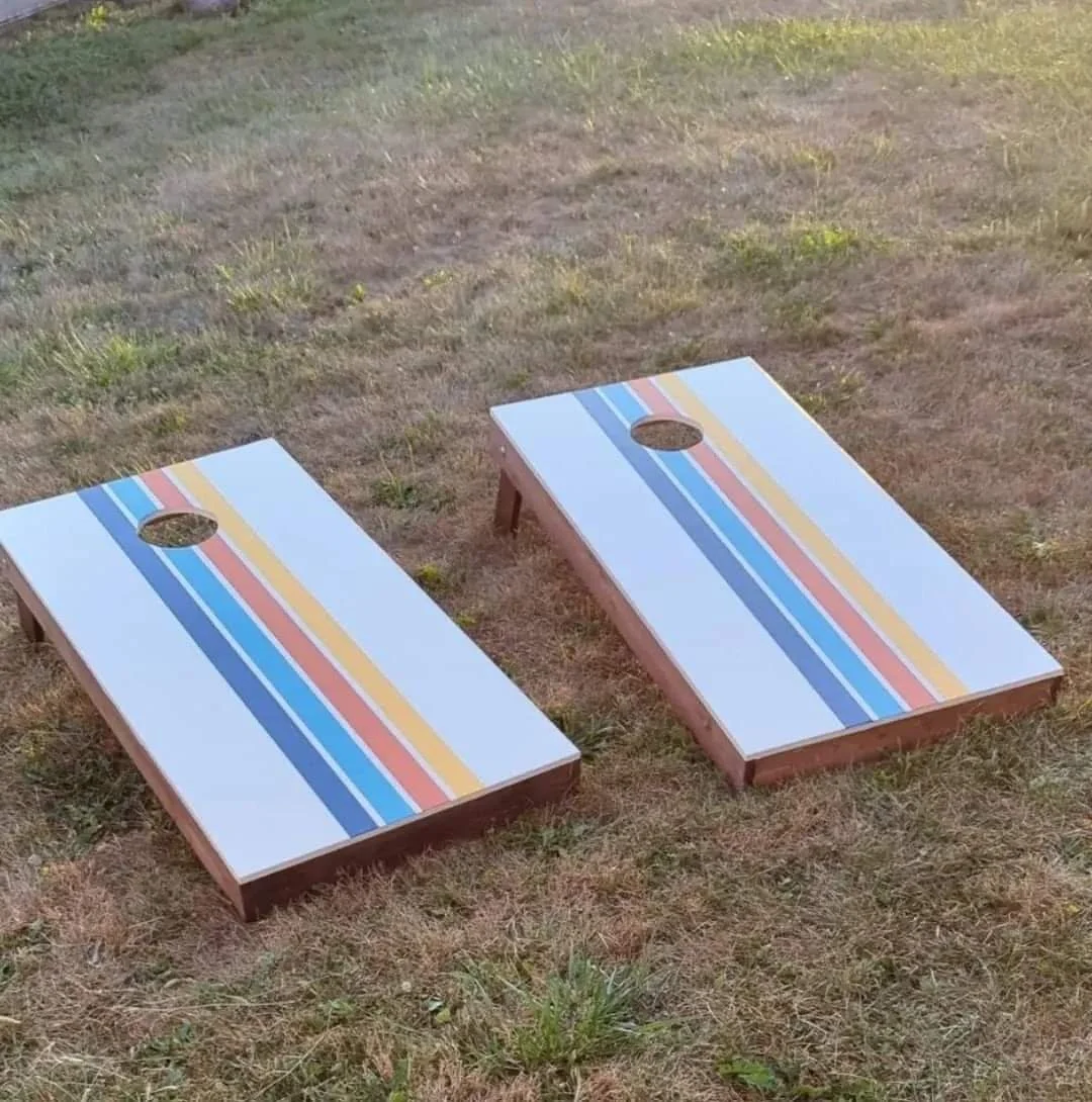 Two cornhole boards with colorful striped designs, placed on the grass.