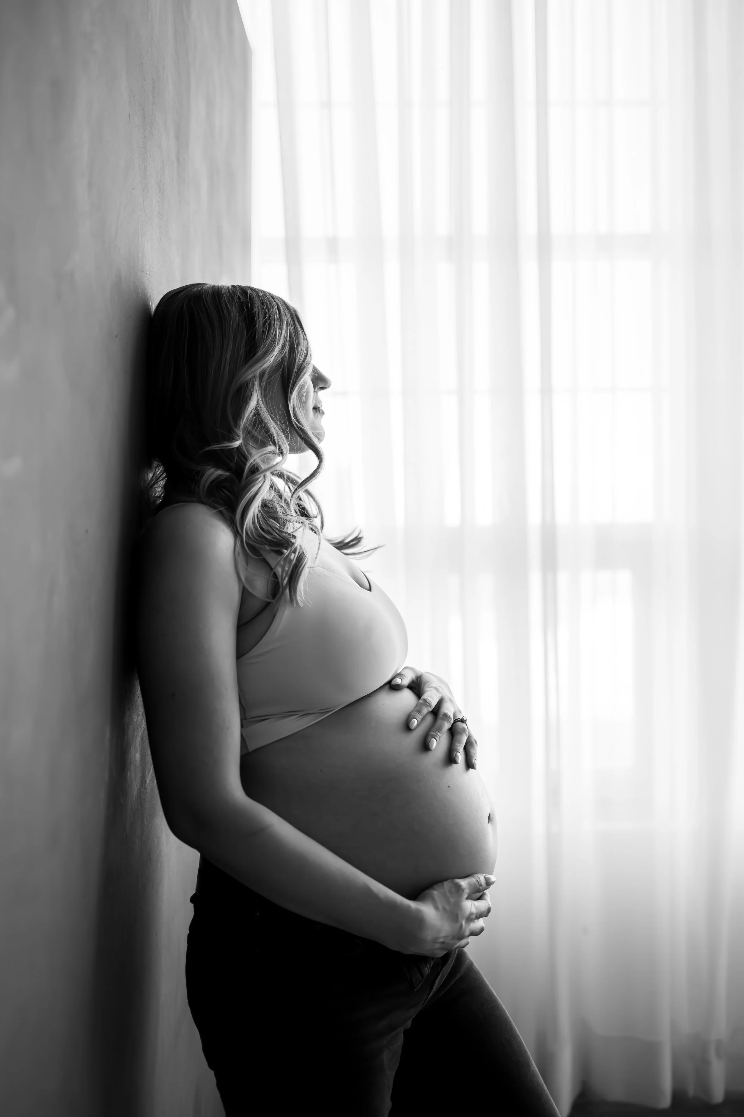 Elegant maternity portrait captured by a Calgary maternity photographer, featuring an expecting mother in a flowing gown holding her baby bump with soft natural light. A timeless pregnancy photoshoot celebrating motherhood and anticipation.