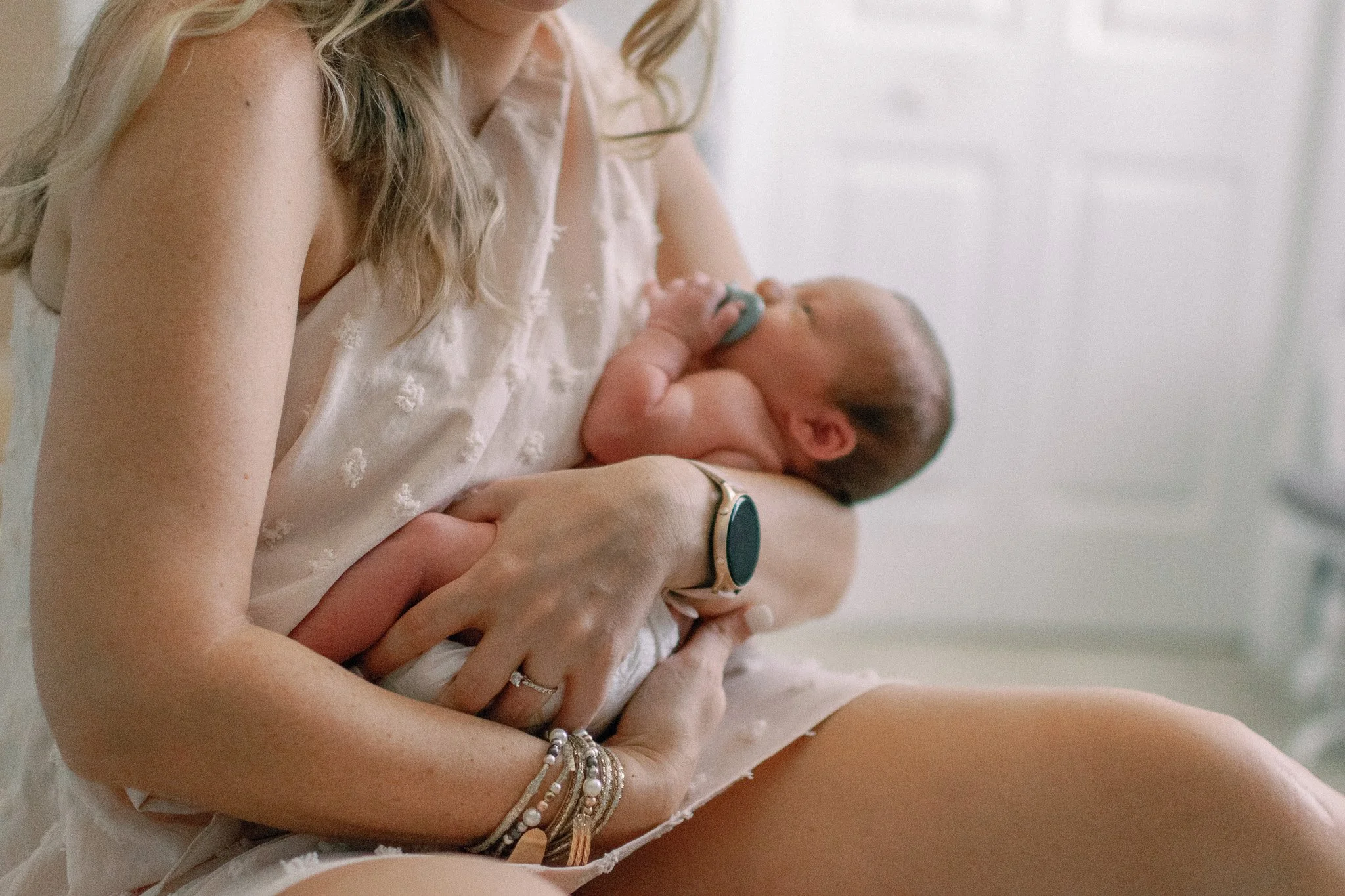 A woman holding a newborn baby in her arms, with the baby's head resting on her chest and using a pacifier.