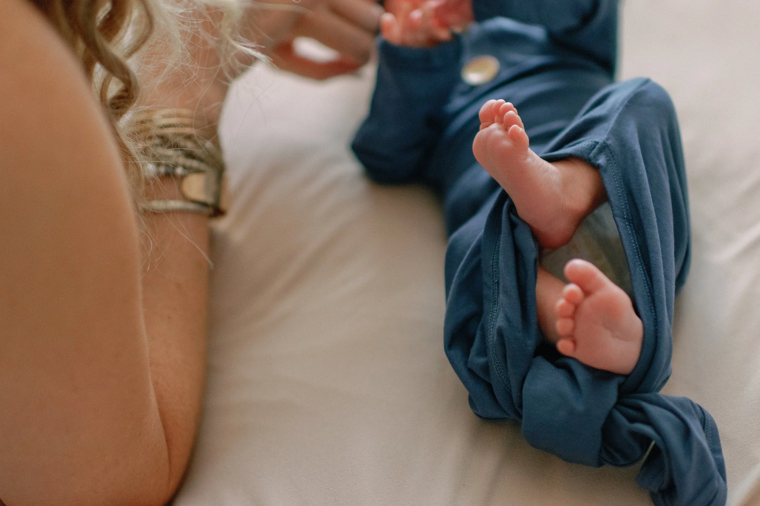 Close-up of a woman's arm and a baby's legs and feet lying on a bed.