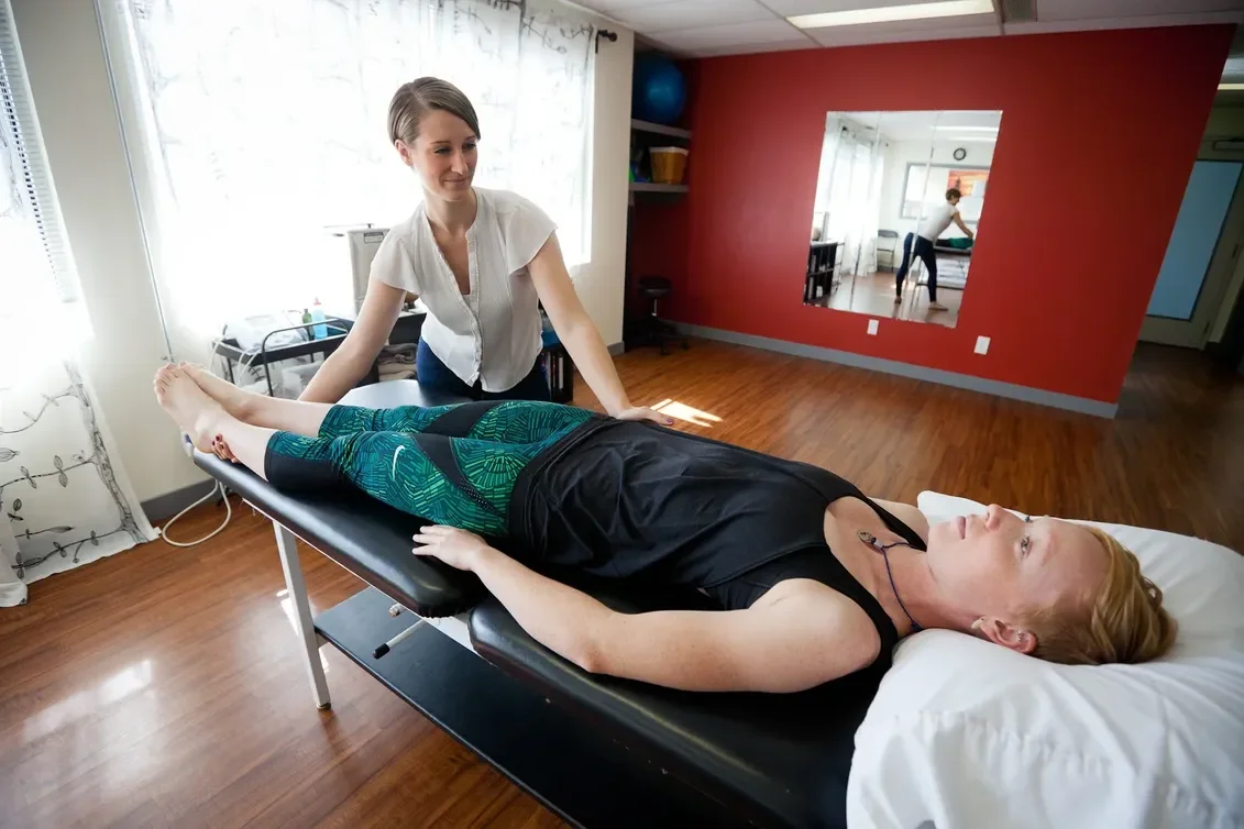 Female physiotherapist performing a medical assessment or physical therapy for back pain on a patient lying on a treatment table in a wellness or therapy room.