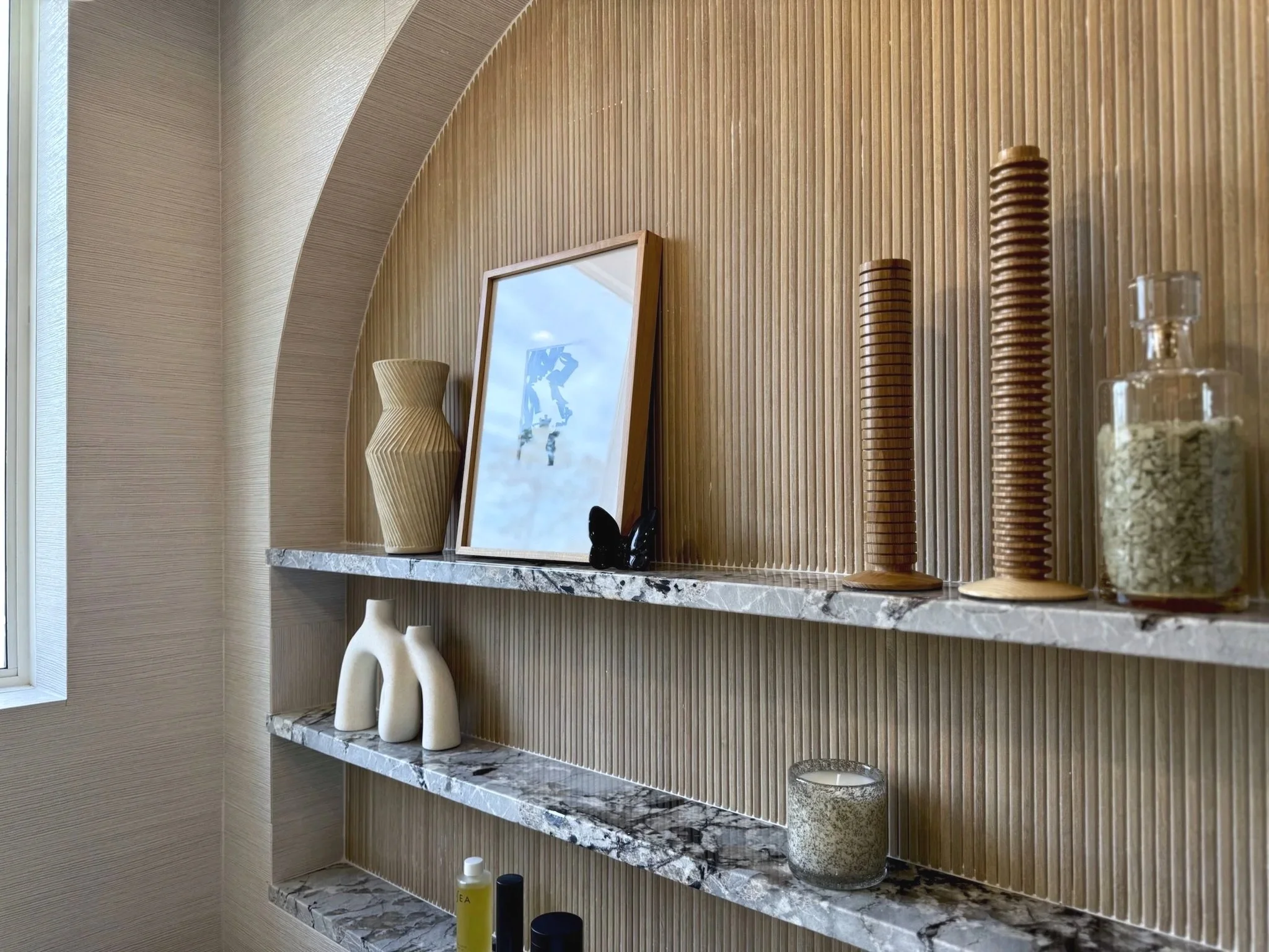 Layered Walls – Phillip Jeffries grasscloth wallpaper softens the room, paired with Porcelanosa’s woven-texture tile for a touch of sheen and glamour.