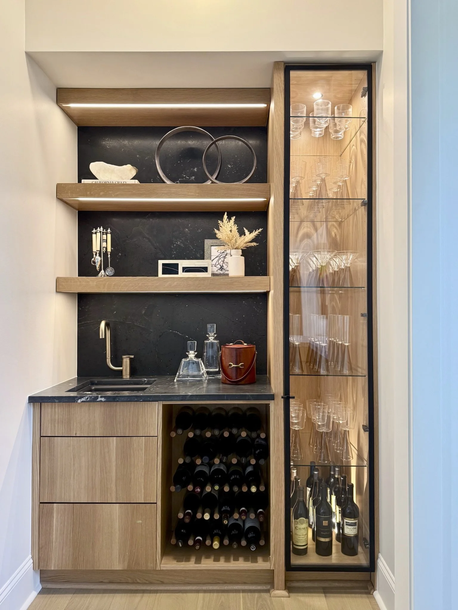 Black leathered stone climbs the walls and covers the countertops in this Kennimer-designed wet bar, with a floor-to-ceiling glass cabinet bringing the sparkle.
