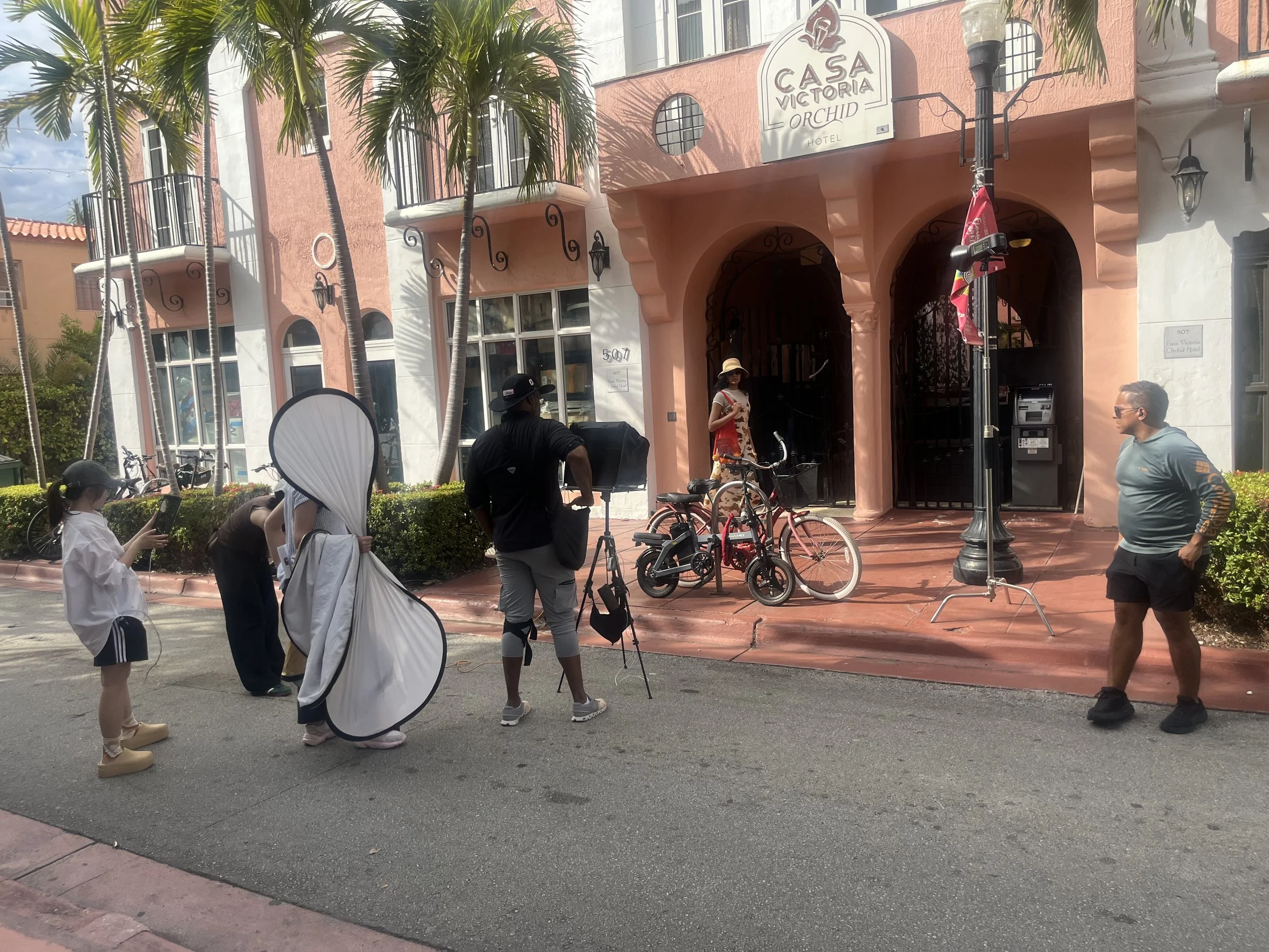 Exterior of Casa Victoria Orchid Hotel with palm trees, bicycles, and people on the sidewalk.
