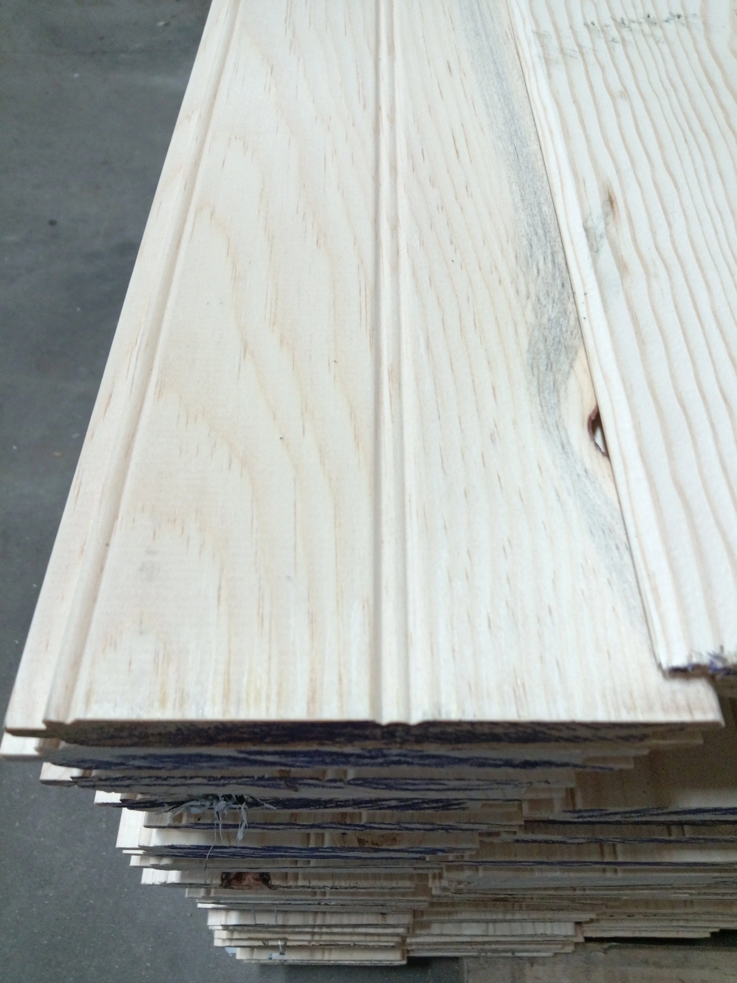 Stack of unfinished wooden planks with visible grain and knots on a concrete floor.