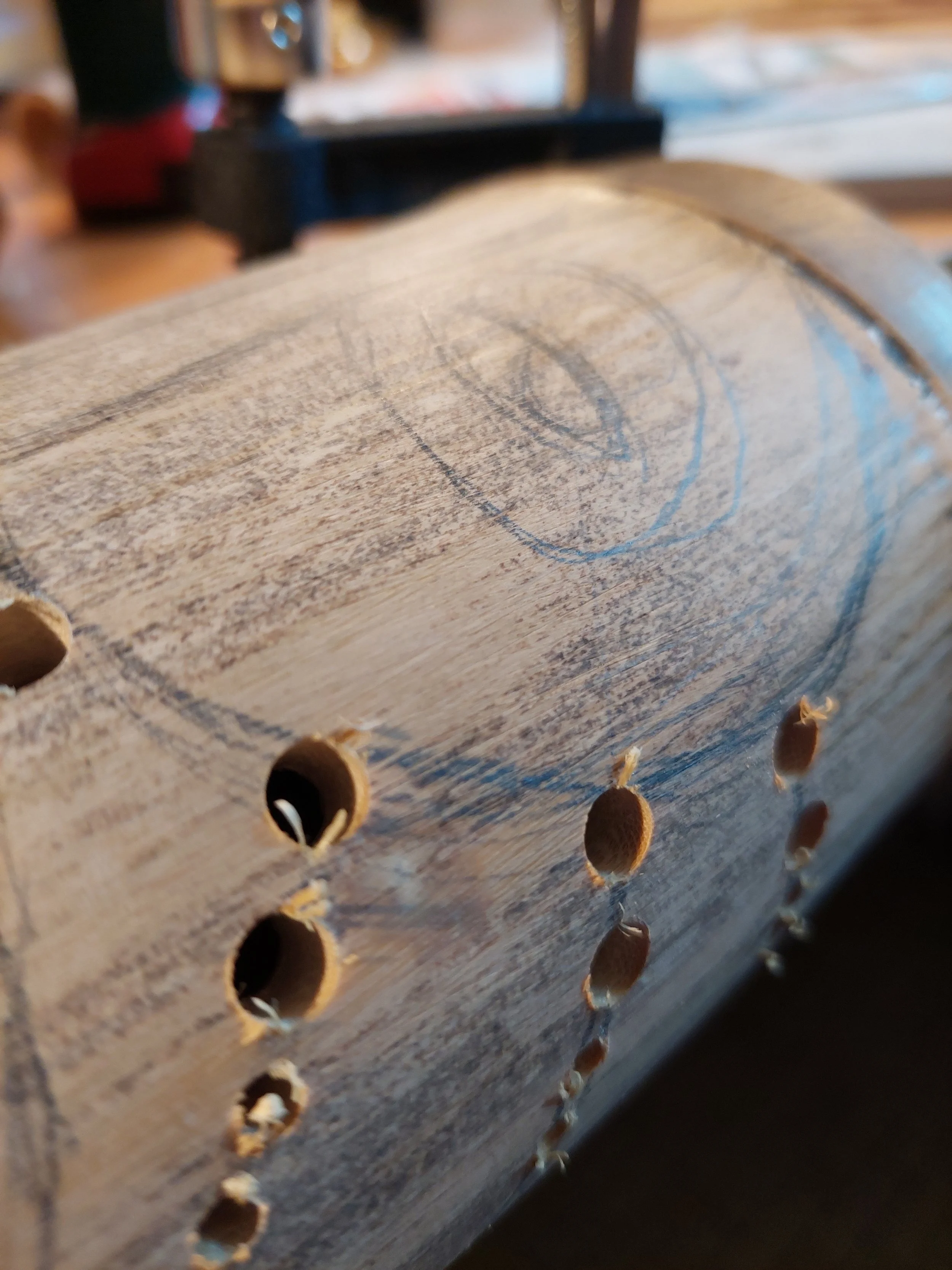 Un morceau de bois avec des trous percés et un dessin ovalé tracé dessus.