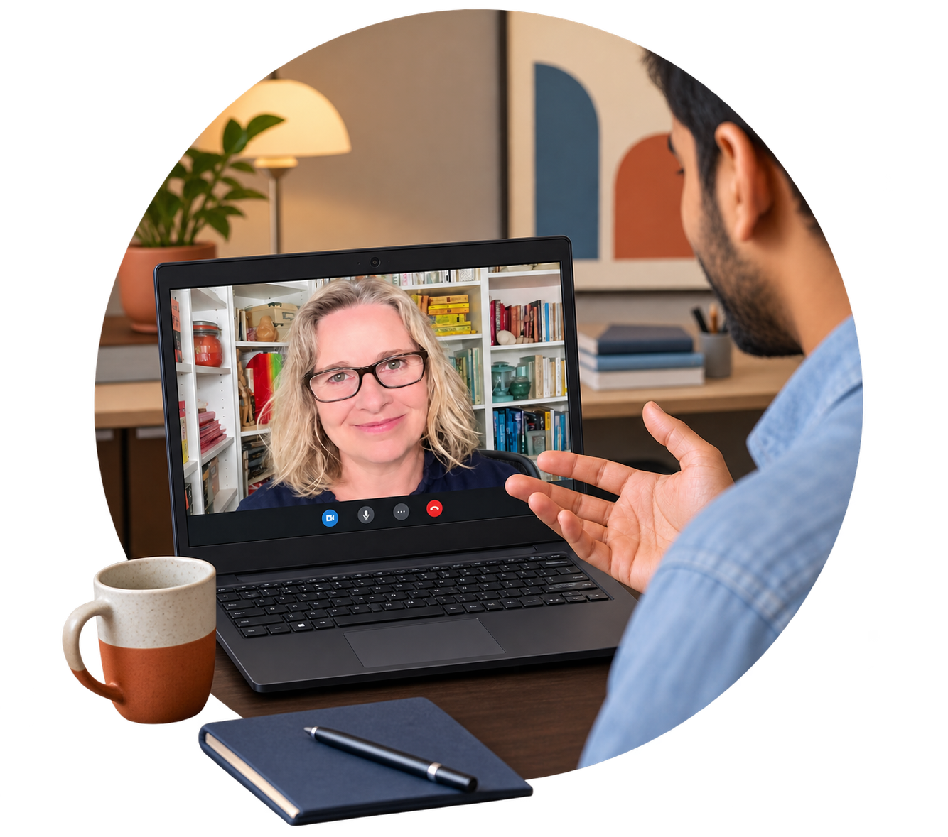 A man is having a video call on his laptop with Judy Wearing who is smiling and wearing glasses. The background shows a shelf with books. The scene is set on a desk with a coffee mug, a closed notebook, and a pen.