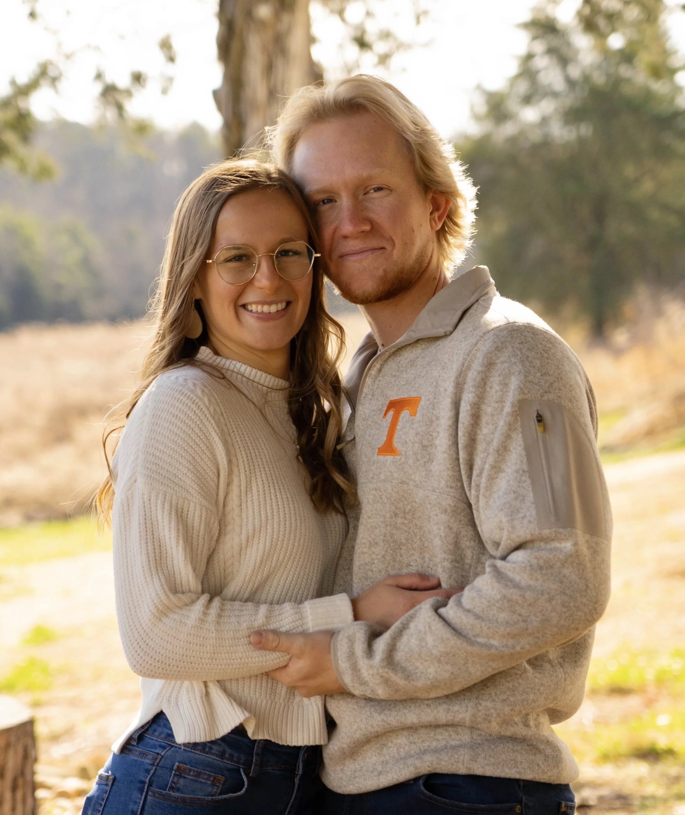a blonde white man and a blonde white woman smile with arms around each other in a sunny outdoor scene