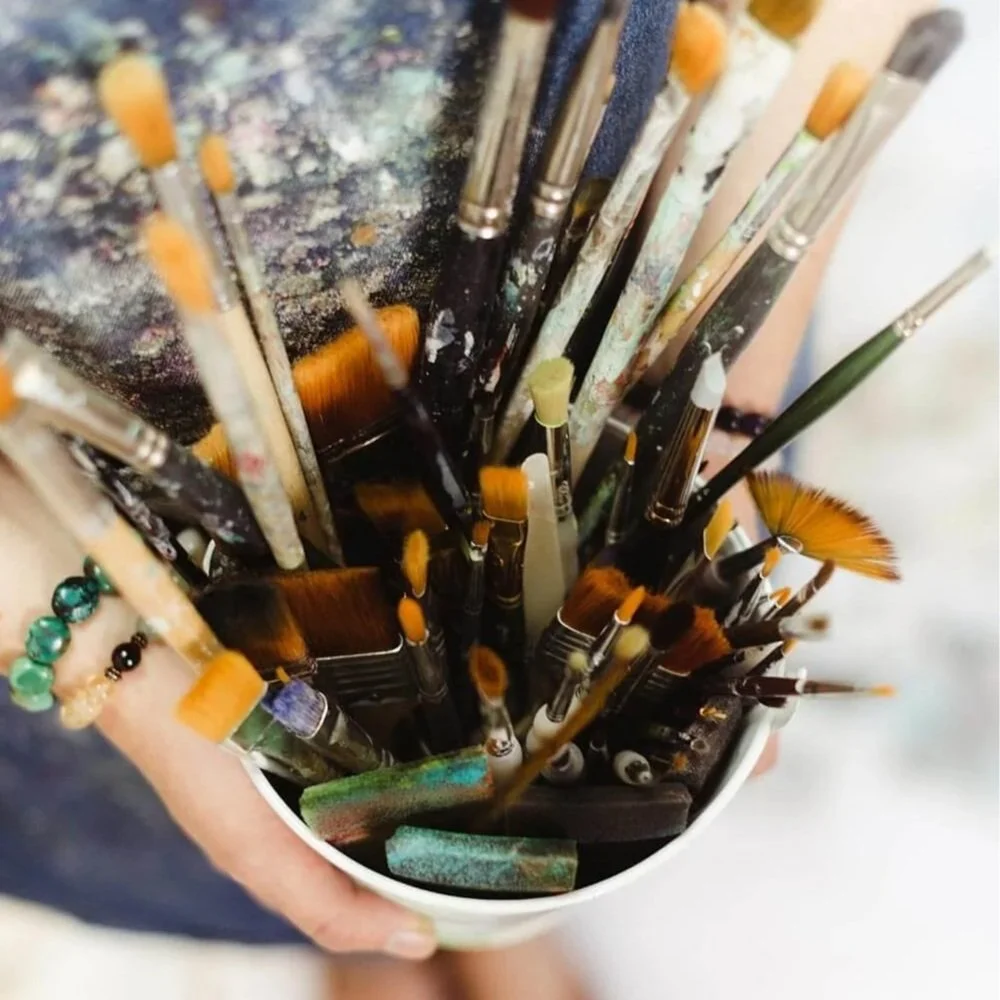 Mixed media art tools including paint brushes, palette knives and sponges.