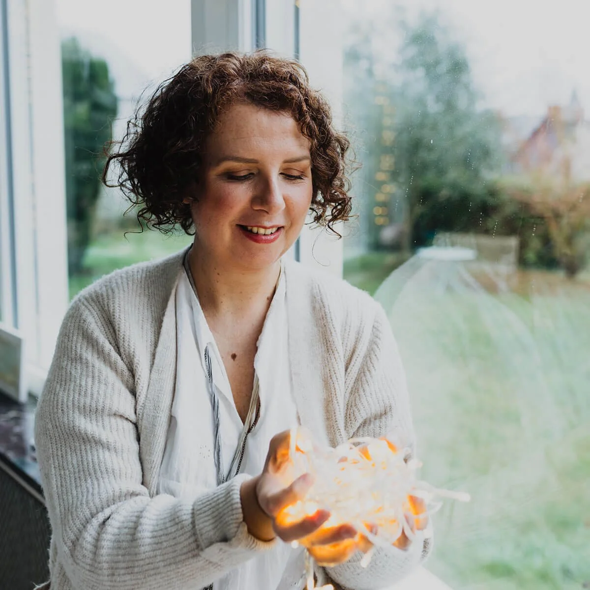 Artist Laly Mille holding fairy lights with a golden glow in her hands