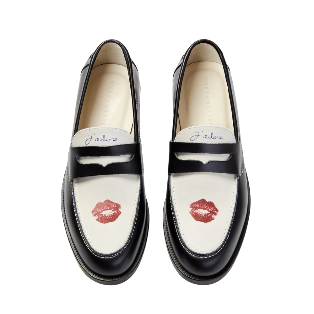 Pair of black and white loafers with a red lipstick kiss and the phrase 'J'adore' on the tongue.