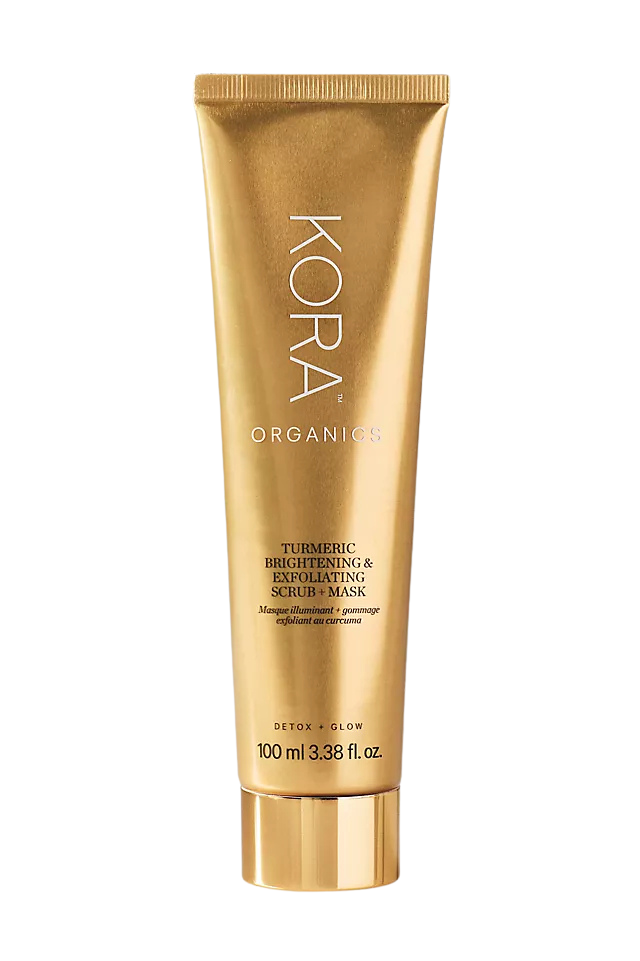 A gold-colored tube of KORA Organics Turmeric Brightening & Exfoliating Scrub + Mask with a black background.