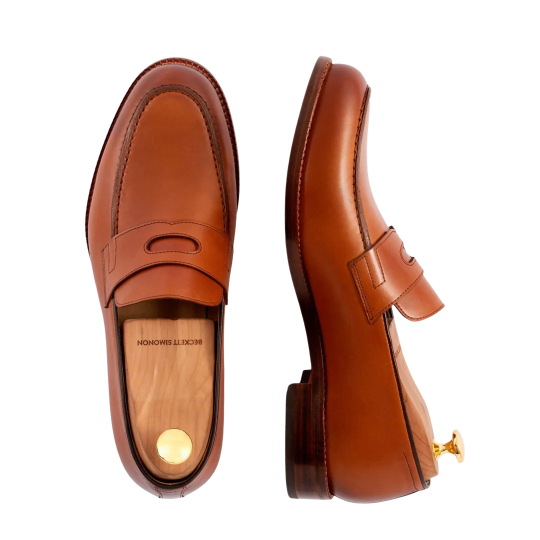 Brown leather dress shoes with slip-on design, placed with the top view of one shoe and a side view of the other, featuring a wooden insole and a gold heel cap.