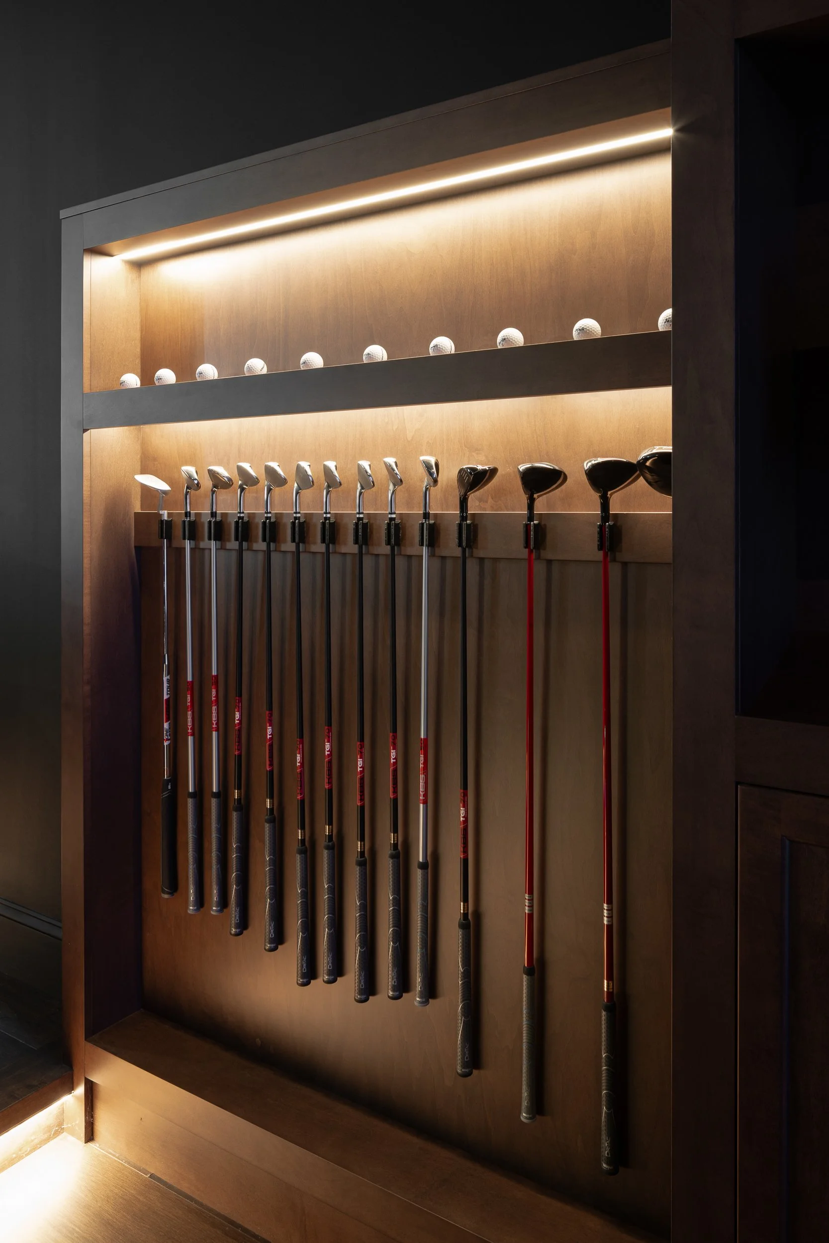 Interior design of a display of golf clubs and golf balls on a wooden wall with lighting.