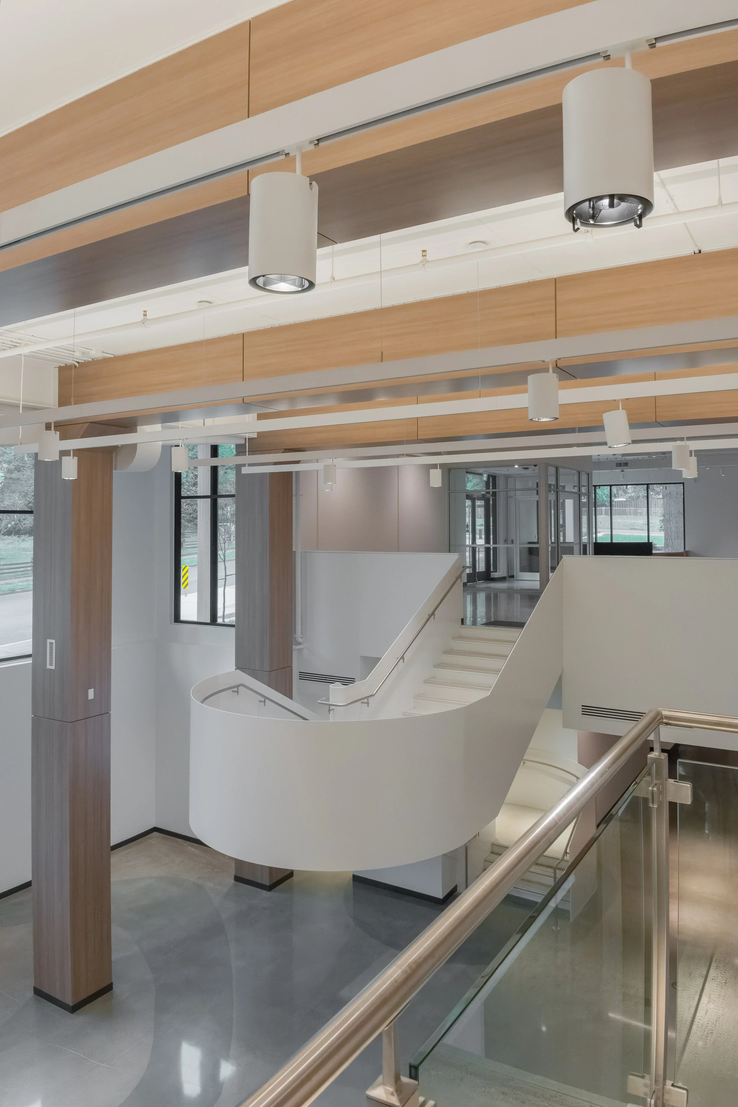 Interior design of a Modern gallery interior space with white staircase, wooden ceiling beams, large windows, and hanging cylindrical lights.