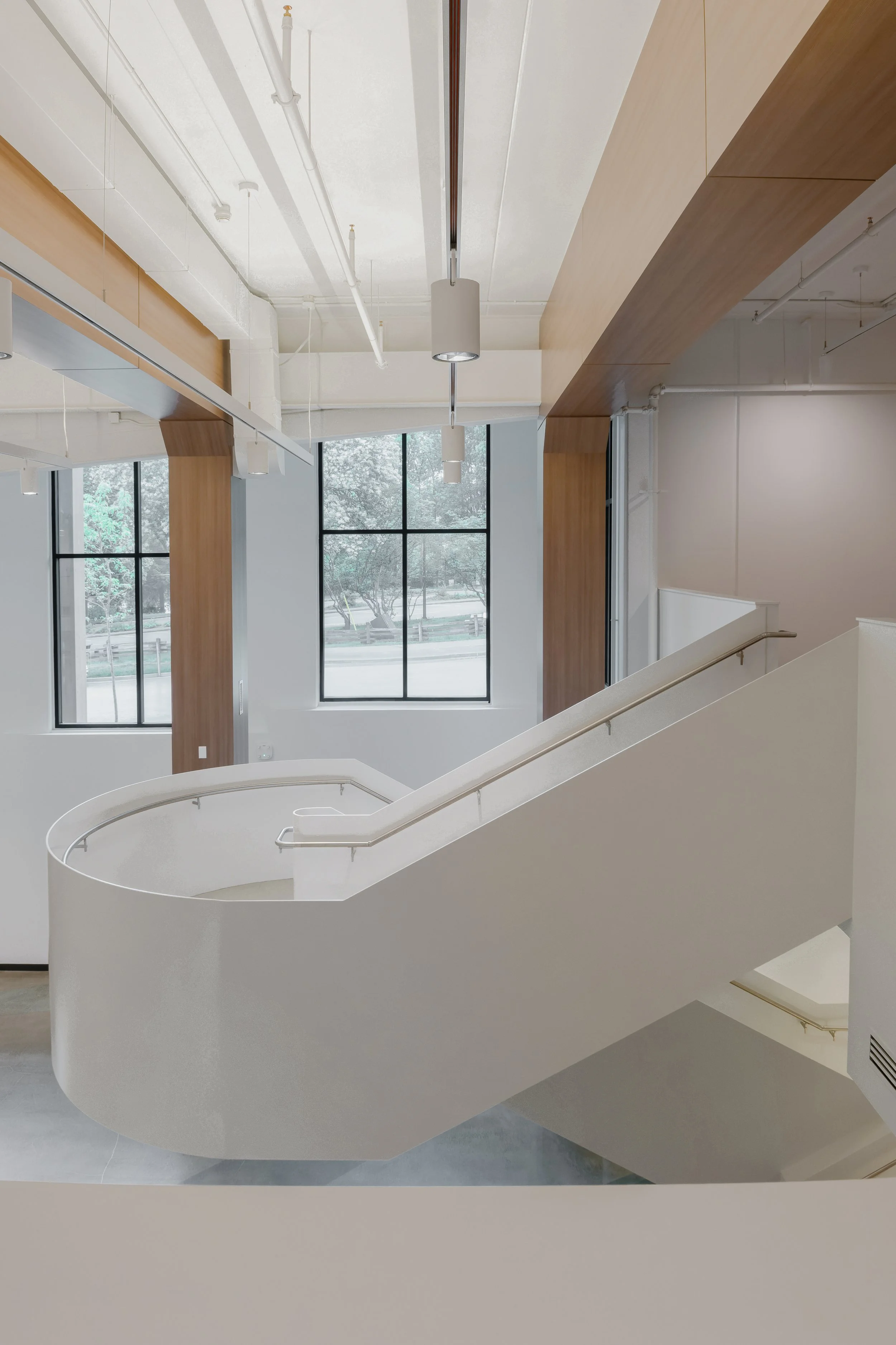Interior design of a Modern interior of a building featuring a curved staircase with white walls, large windows, and wooden accents on the ceiling and walls.