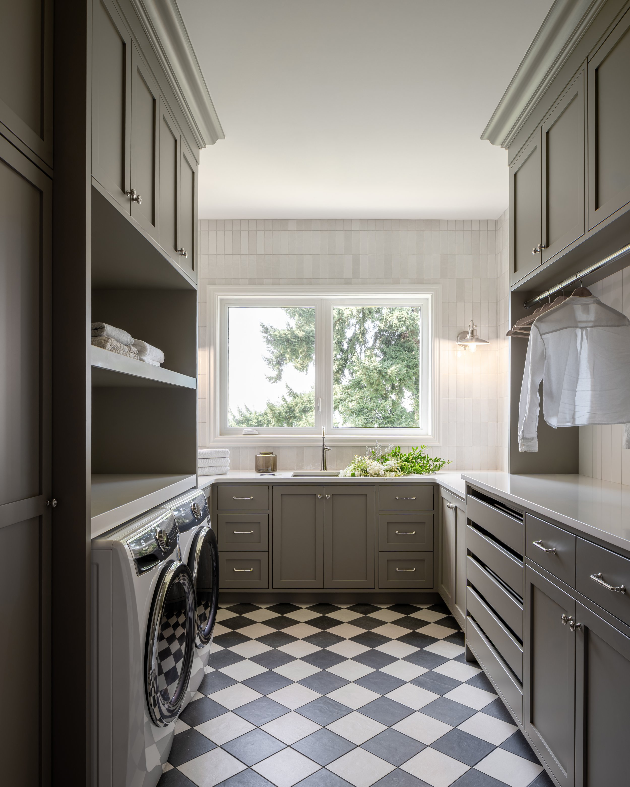 Interior design of a Laundry room with gray cabinets, a window, and a black and white checkered floor.