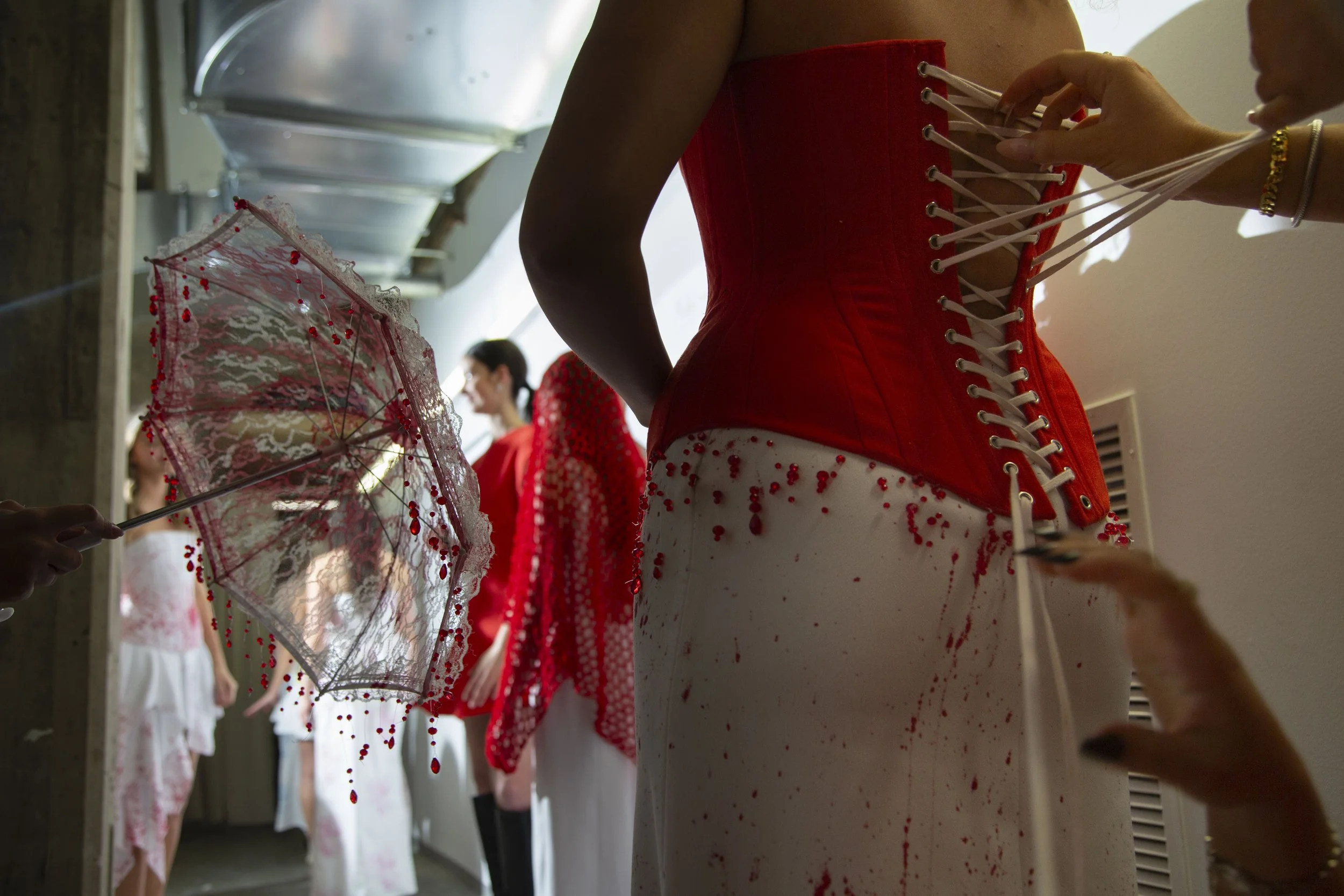 8.	Fellow designers assist Layla in tightening corset strings during the senior fashion show. Models needed to walk for multiple designers, sometimes leaving only a few minutes to complete a full outfit change.