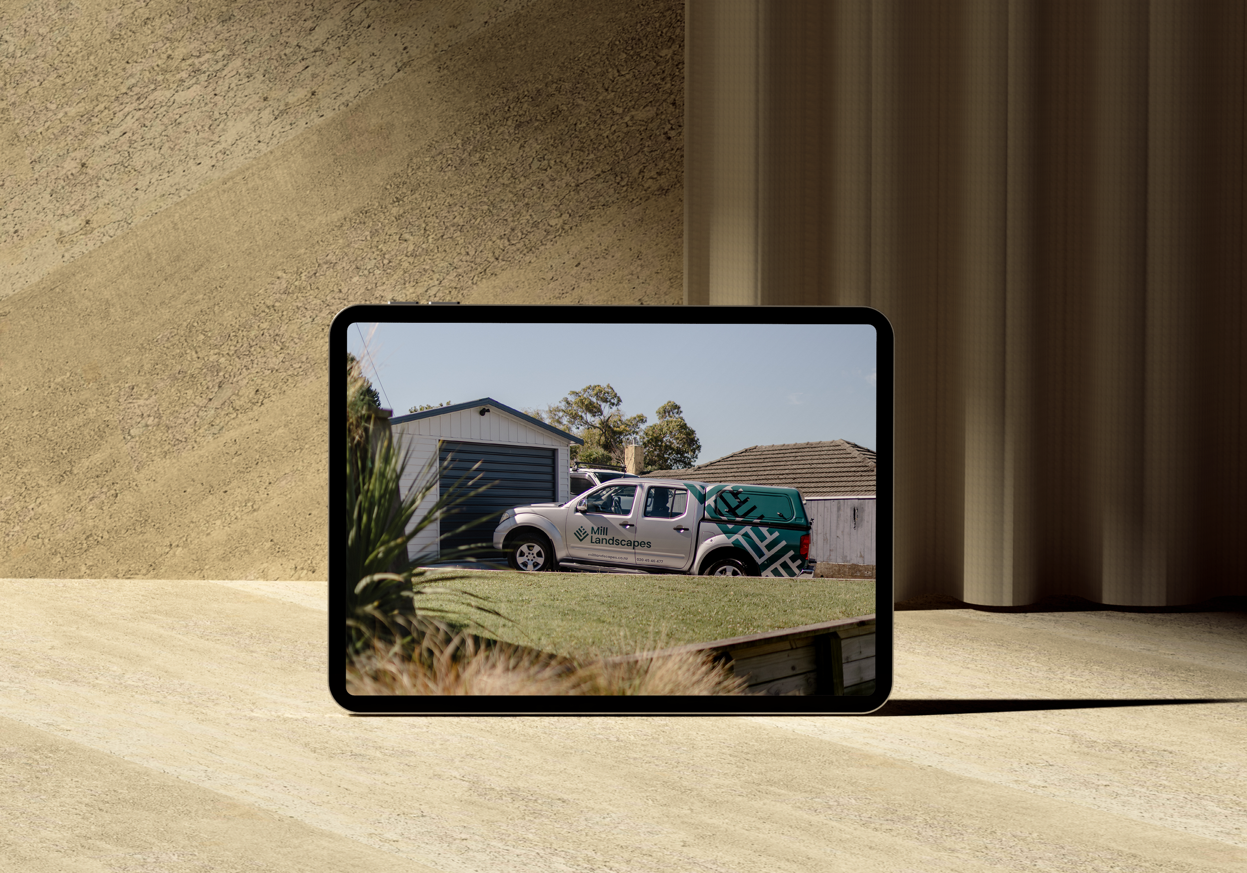 A tablet displaying a photo of landscaping equipment vehicle parked in front of a house with grass and trees.