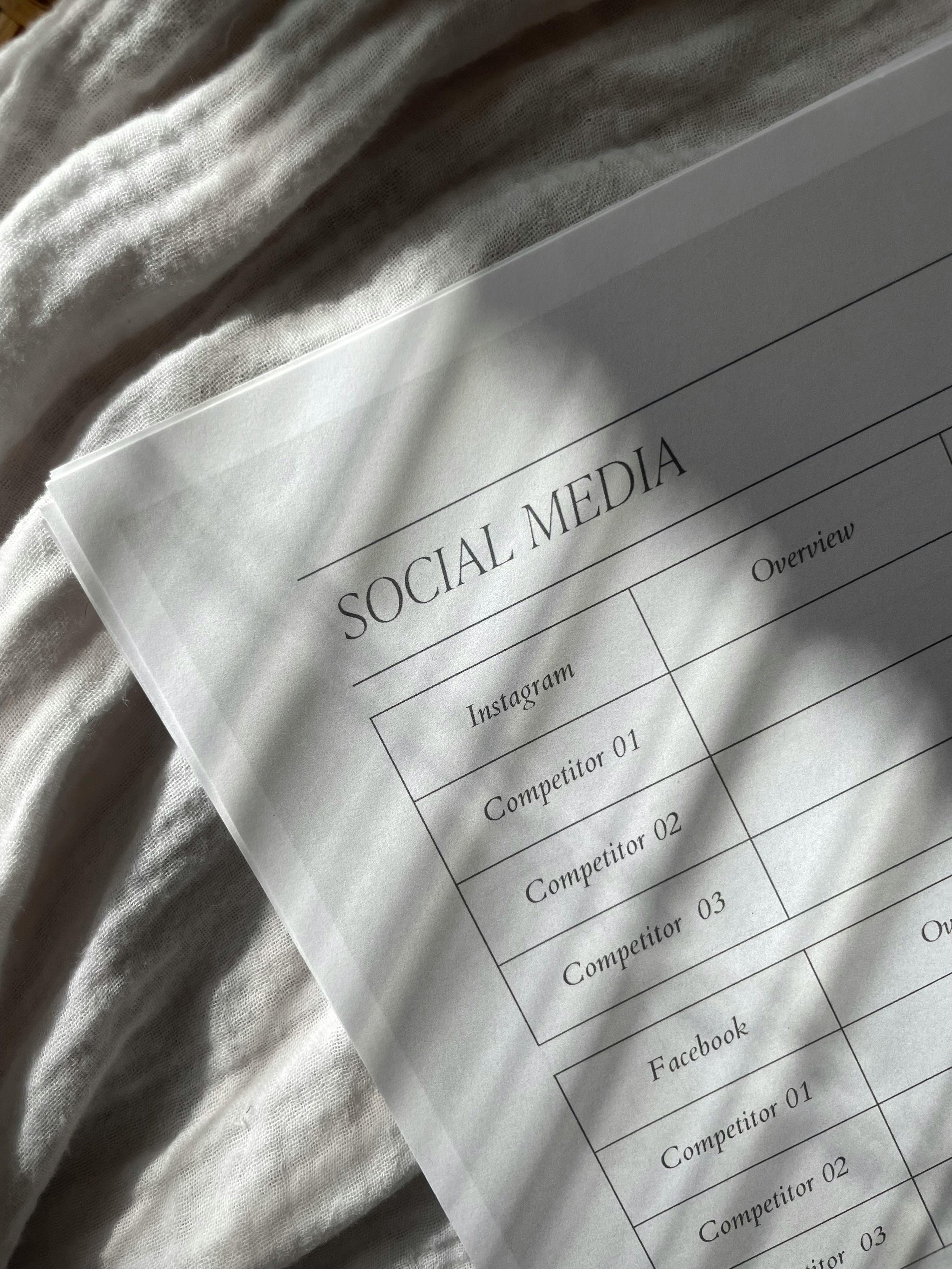 A printed social media comparison chart on white paper, placed on light-colored fabric.